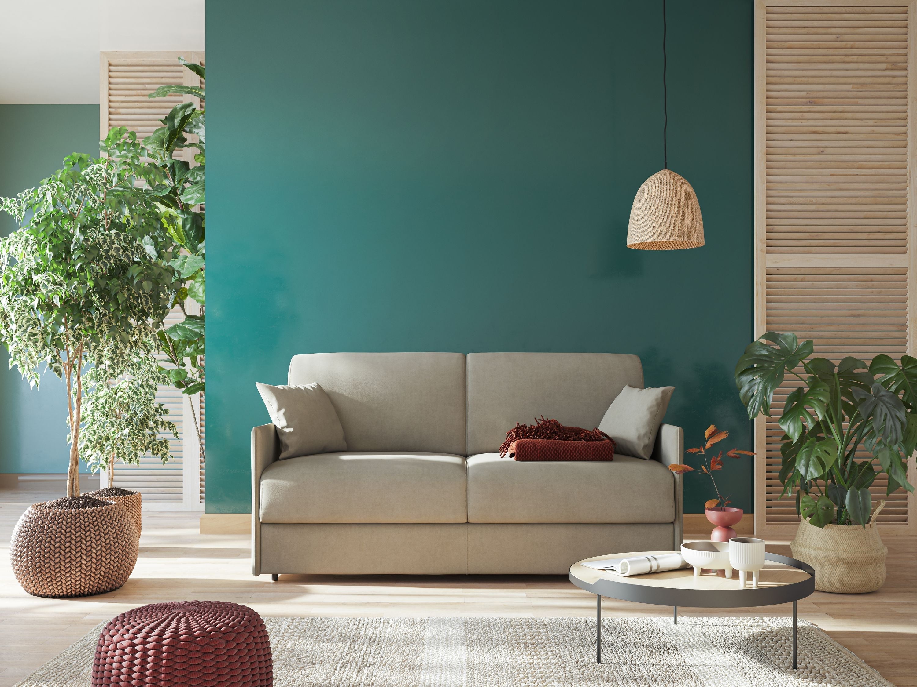 Un soggiorno moderno con un divano grigio chiaro, una parete decorativa verde, cuscini beige, un tavolino rotondo, piante da interno, un cestino intrecciato e una lampada a sospensione illuminata da una tenue luce naturale.