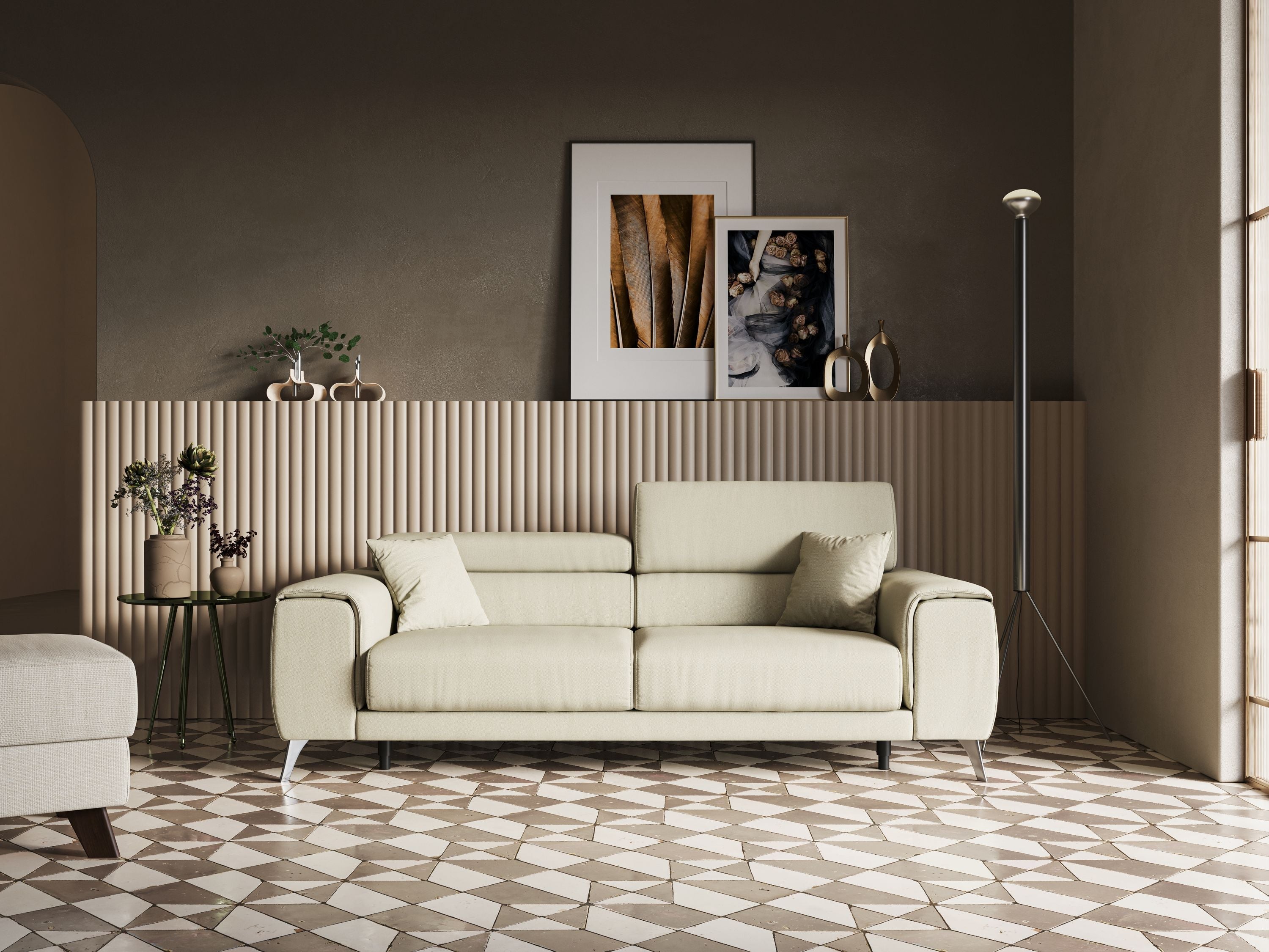 Un soggiorno moderno con un divano beige chiaro, pavimento in piastrelle geometriche, tavolino con vasi, lampada da terra alta e due stampe artistiche incorniciate su una parete color tortora con pannelli verticali. La luce del sole filtra a fiotti.