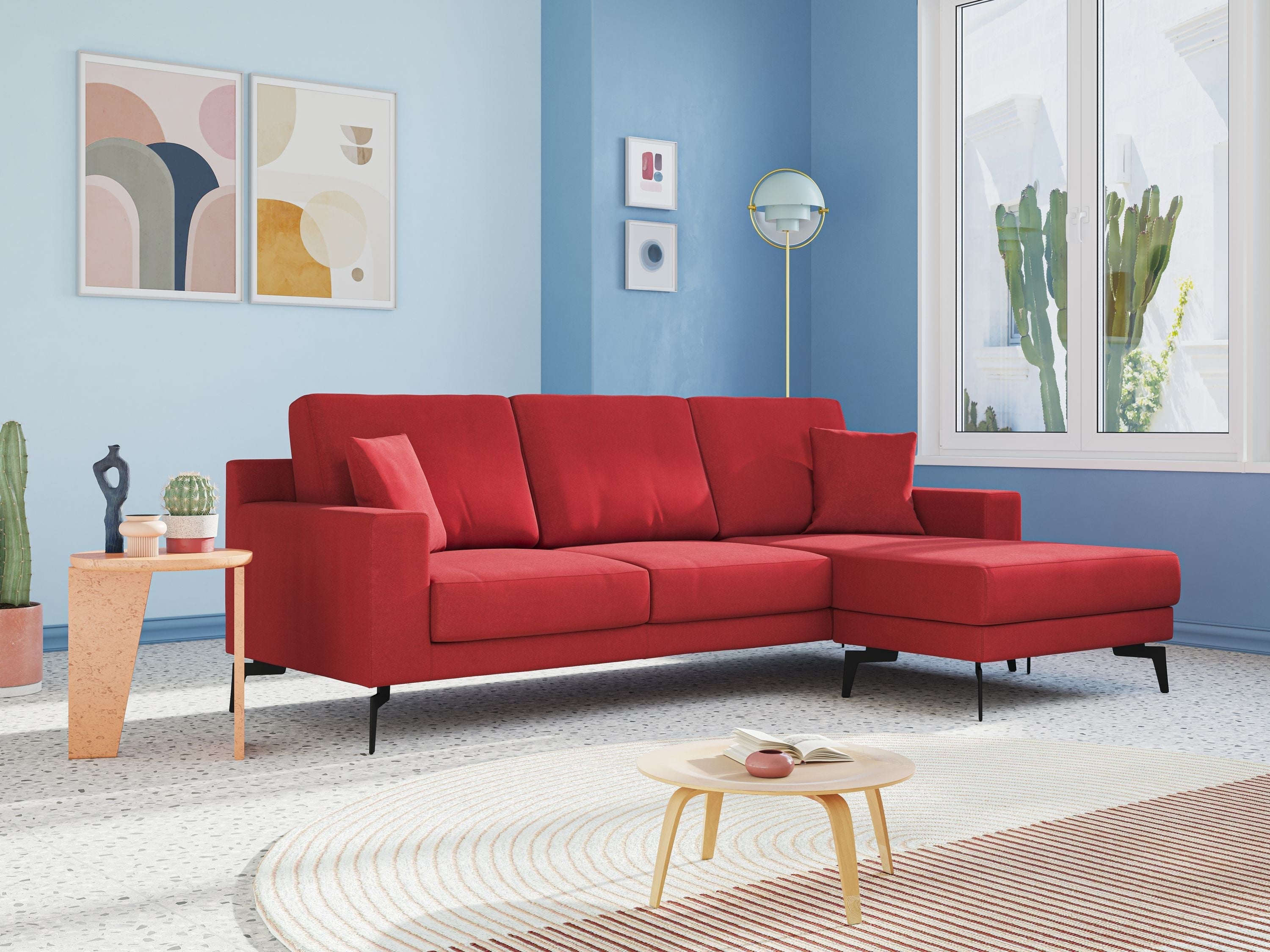 Un soggiorno moderno con un divano componibile rosso, pareti azzurre, opere d'arte astratte, cactus in vaso, un tavolino rotondo, una lampada da terra e una grande finestra che lascia entrare la luce naturale.