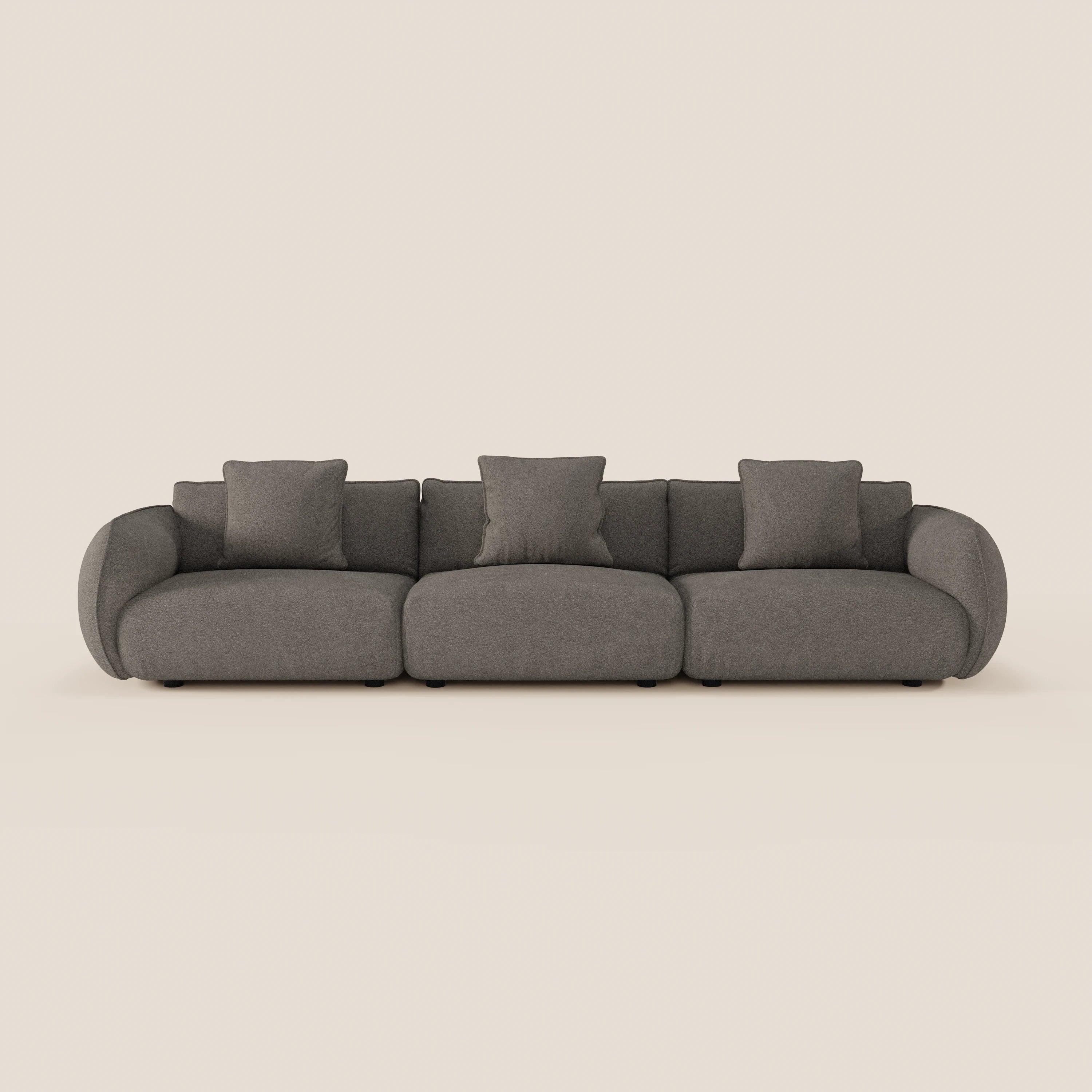 Il divano modulare a 3 sedute Nimbus di Divani.Store è un moderno divano grigio scuro con braccioli arrotondati, tre cuscini di seduta e cinque cuscini quadrati coordinati, su sfondo beige chiaro. Rivestito in morbido tessuto antimacchia effetto cotone T33.