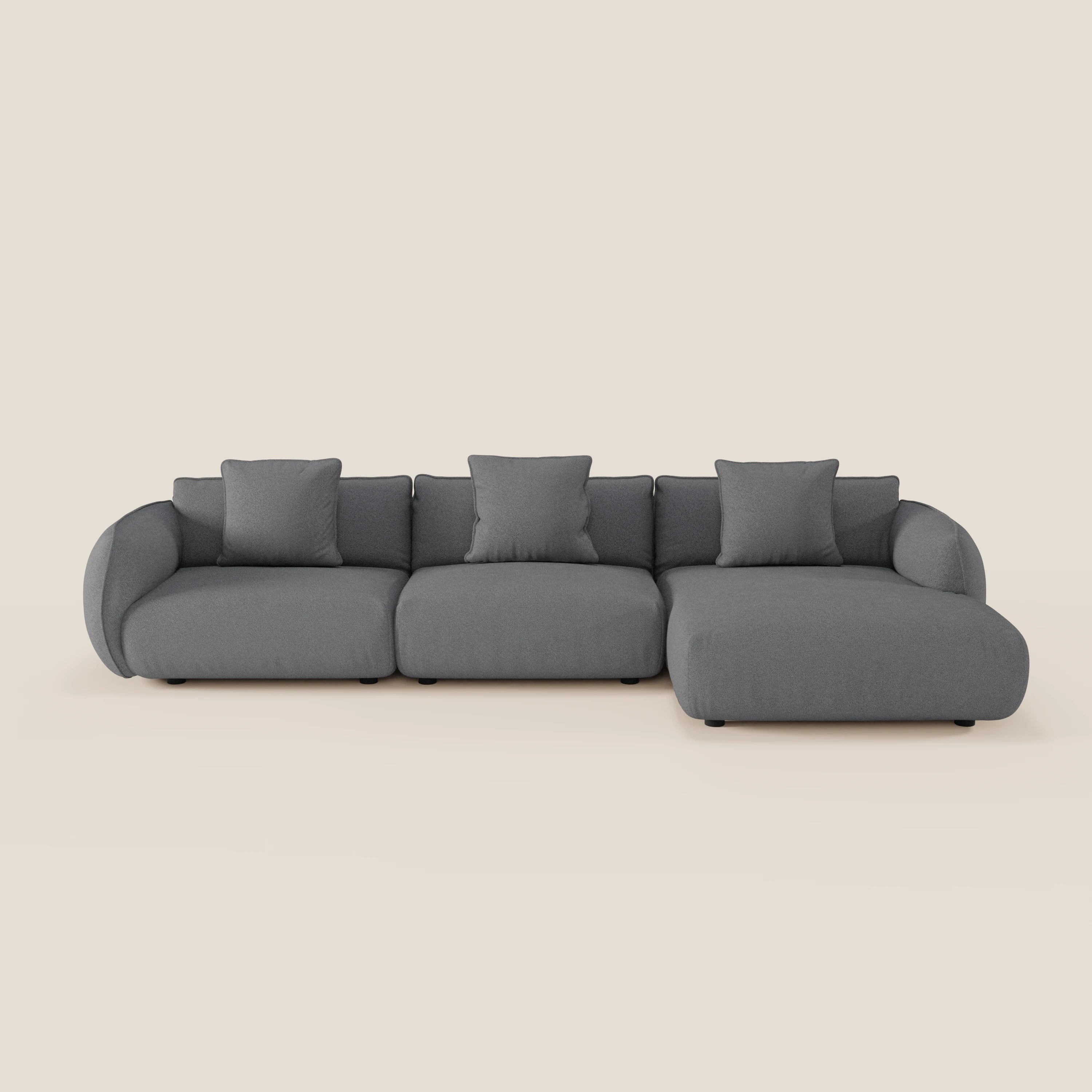 Il divano Nimbus angolare con penisola componibile di Divani.Store è un moderno divano grigio a 3 posti con chaise longue destra, braccioli curvi, quattro cuscini quadrati e piedini neri in tessuto effetto cotone smacchiabile.