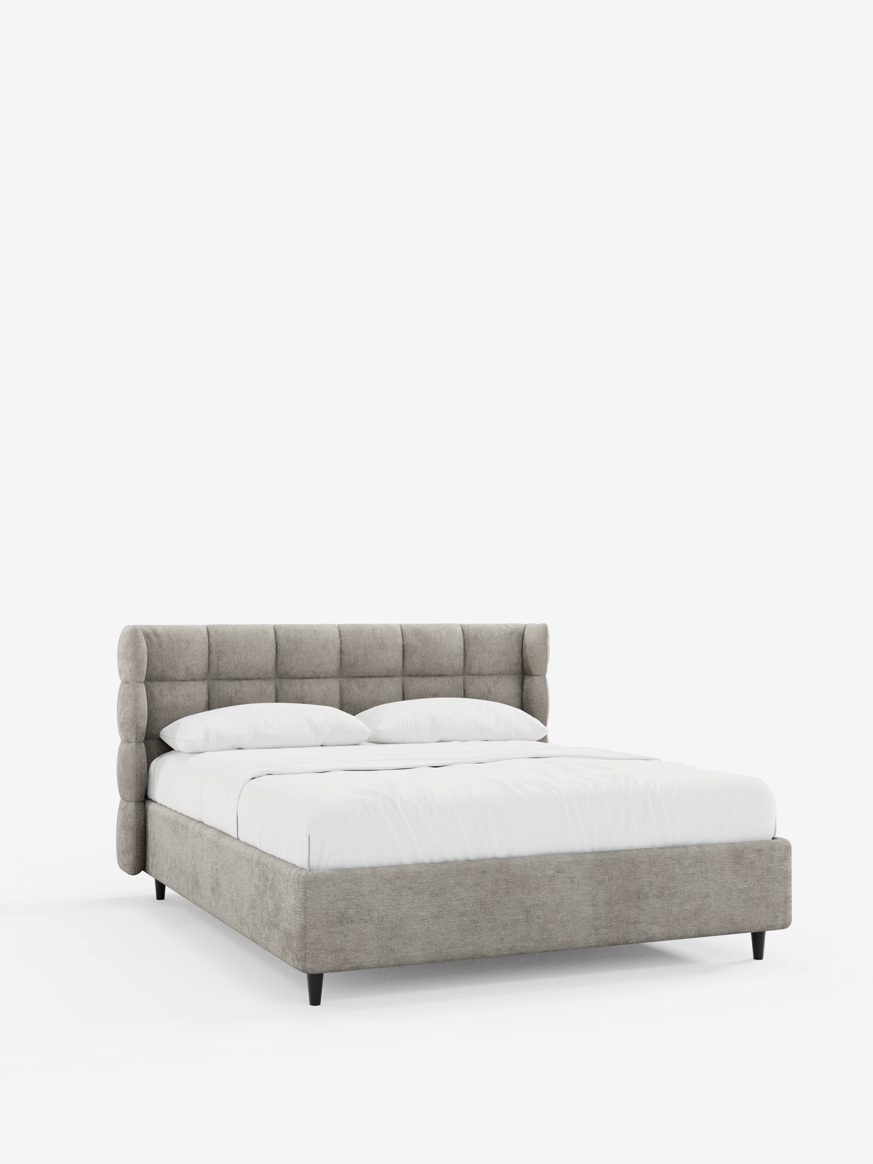 Il moderno letto imbottito RAGNAR con contenitore e testiera capitonné avvolgente di Letti.store, rivestito in tessuto grigio chiaro certificato Oeko-Tex®, presenta un’elegante testiera cilindrica capitonné. Il letto è abbinato a un set di lenzuola bianche a tinta unita e due cuscini, e poggia a terra su corte gambe nere, in contrasto con uno sfondo bianco candido.