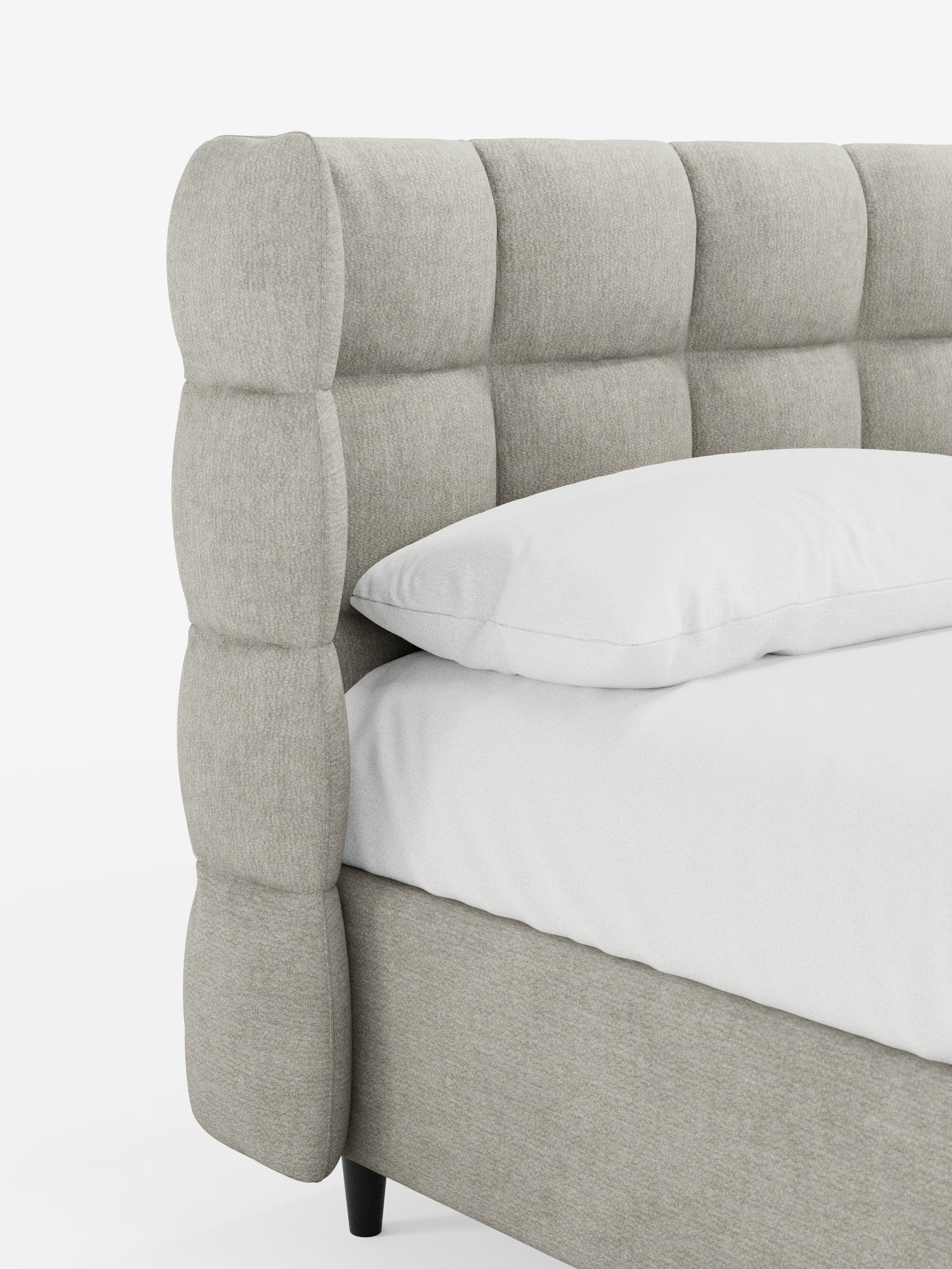 Primo piano di un letto imbottito RAGNAR con contenitore e testiera capitonné avvolgente di Letti.store, caratterizzato da un’elegante testiera in tessuto capitonné color beige chiaro, certificata Oeko-Tex®, con motivo a griglia. Il materasso è rivestito con biancheria da letto bianca e un cuscino bianco, mentre la struttura del letto è in tinta con la testiera. Lo sfondo è bianco a tinta unita.