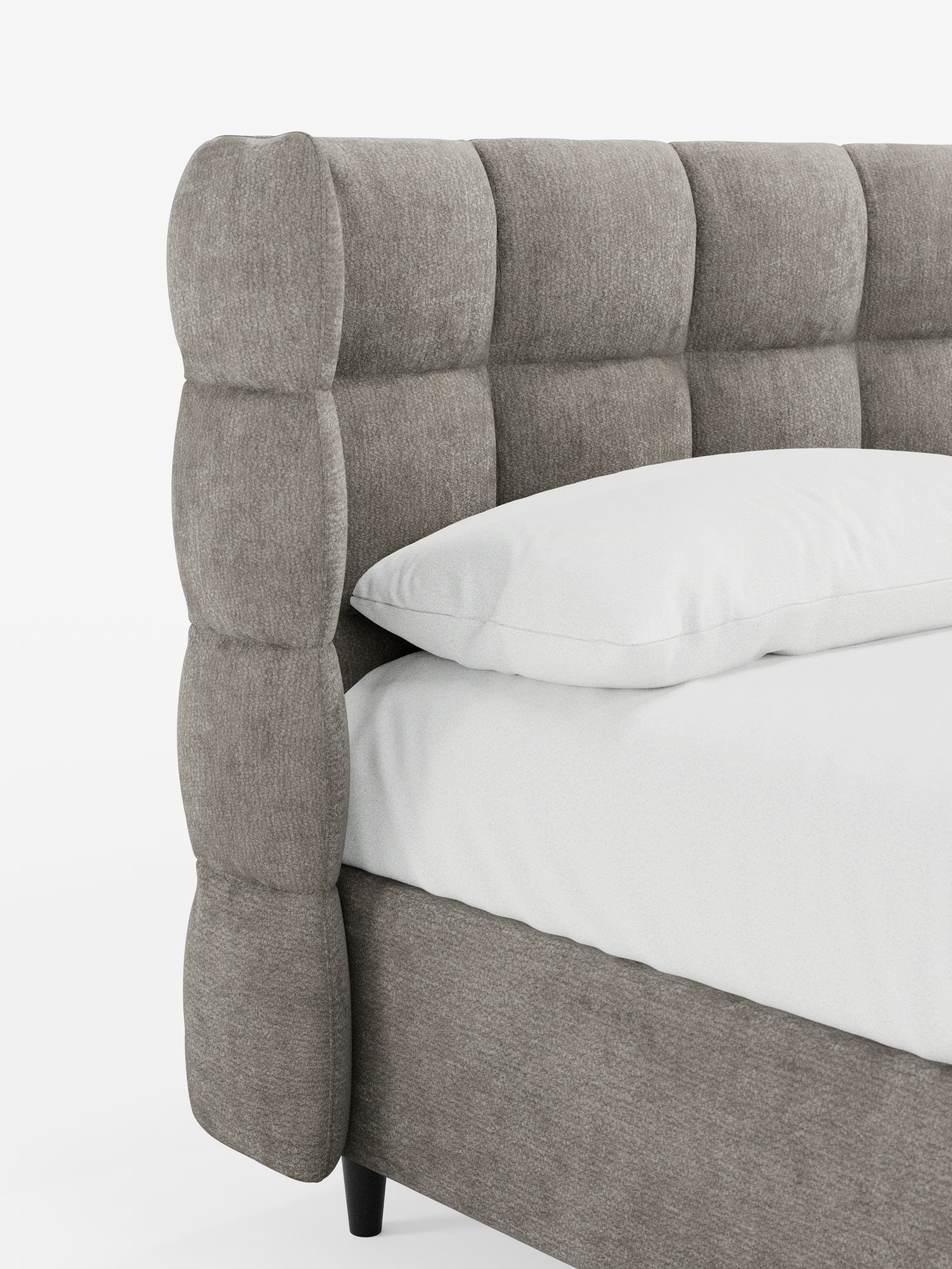 Primo piano del letto imbottito RAGNAR con contenitore e testiera capitonné avvolgente di Letti.store, caratterizzato da un’alta testiera capitonné in tessuto grigio chiaro certificato Oeko-Tex®. Il letto è rivestito con un cuscino e un lenzuolo bianchi, che lasciano intravedere l’angolo del materasso e parte della sponda laterale. Le sue corte gambe nere e lo sfondo bianco a tinta unita sottolineano la raffinata eleganza di questo letto imbottito con contenitore.