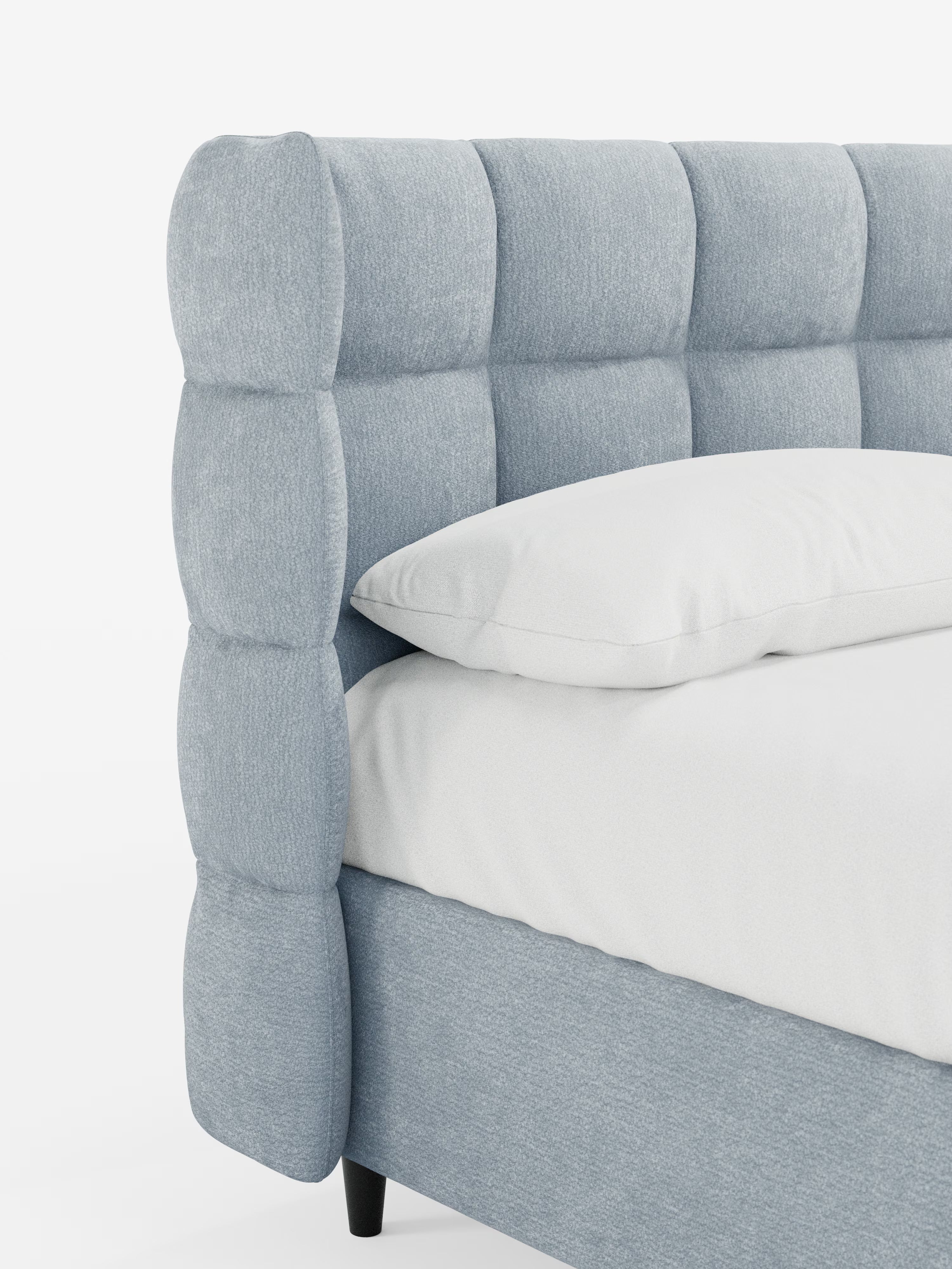 Primo piano del letto imbottito RAGNAR con contenitore e testiera capitonné avvolgente di Letti.store, caratterizzato da una testiera e una base di colore azzurro, con trama a capitonné, realizzate in un elegante tessuto certificato Oeko-Tex®. Il letto, dal design moderno e minimalista, è raffigurato con gambe corte e scure e si staglia su uno sfondo bianco a tinta unita. Un cuscino bianco è appoggiato su un materasso bianco.