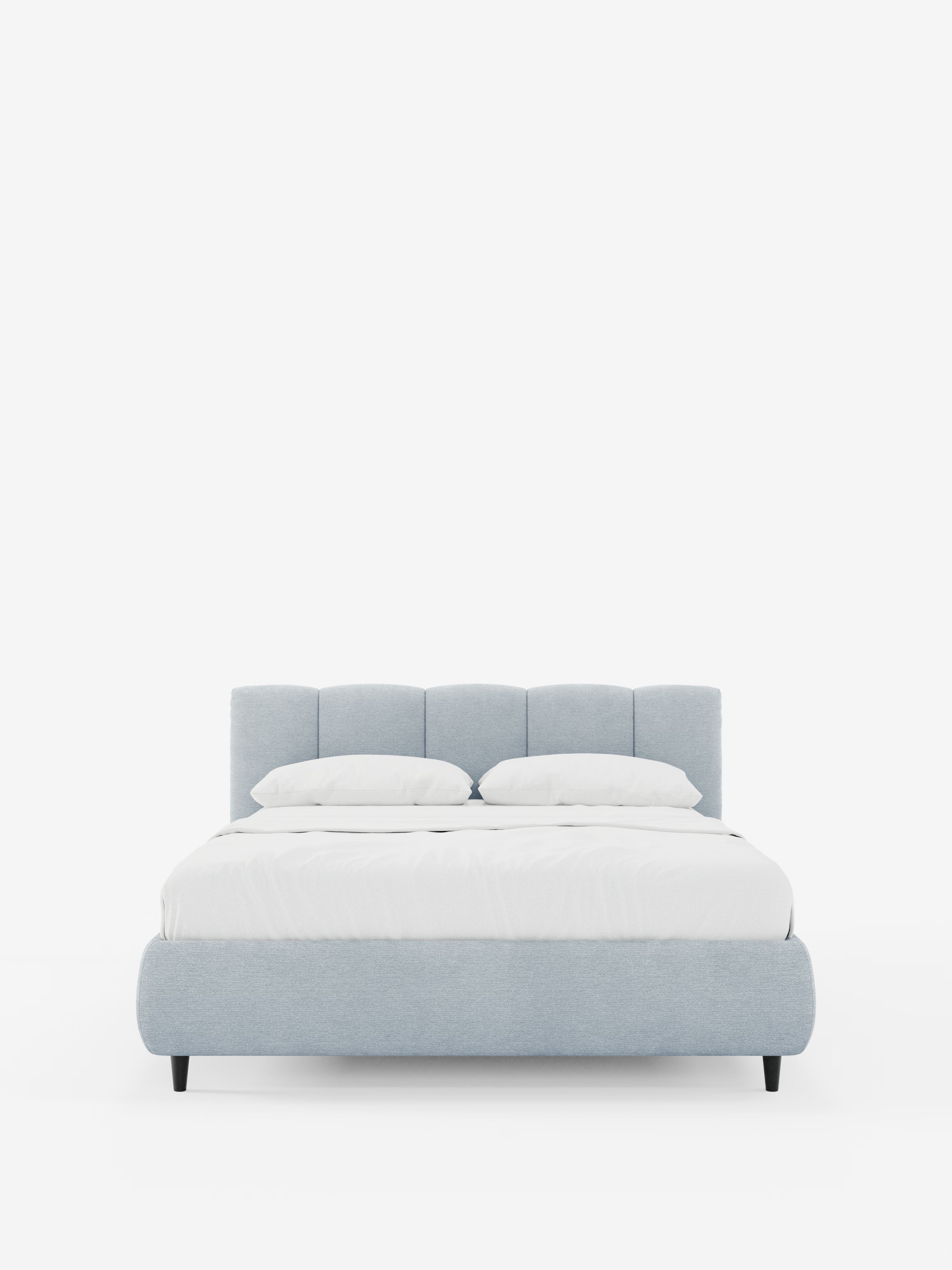 Un letto imbottito ARKAM azzurro con contenitore e testiera a cuciture verticali di Letti.store, rivestito in tessuto certificato Oeko-Tex® e caratterizzato da una testiera con cuciture verticali, due cuscini bianchi e una coperta bianca. Questo letto in stile shabby chic è sostenuto da gambe nere ed è posizionato al centro di uno sfondo bianco a tinta unita.