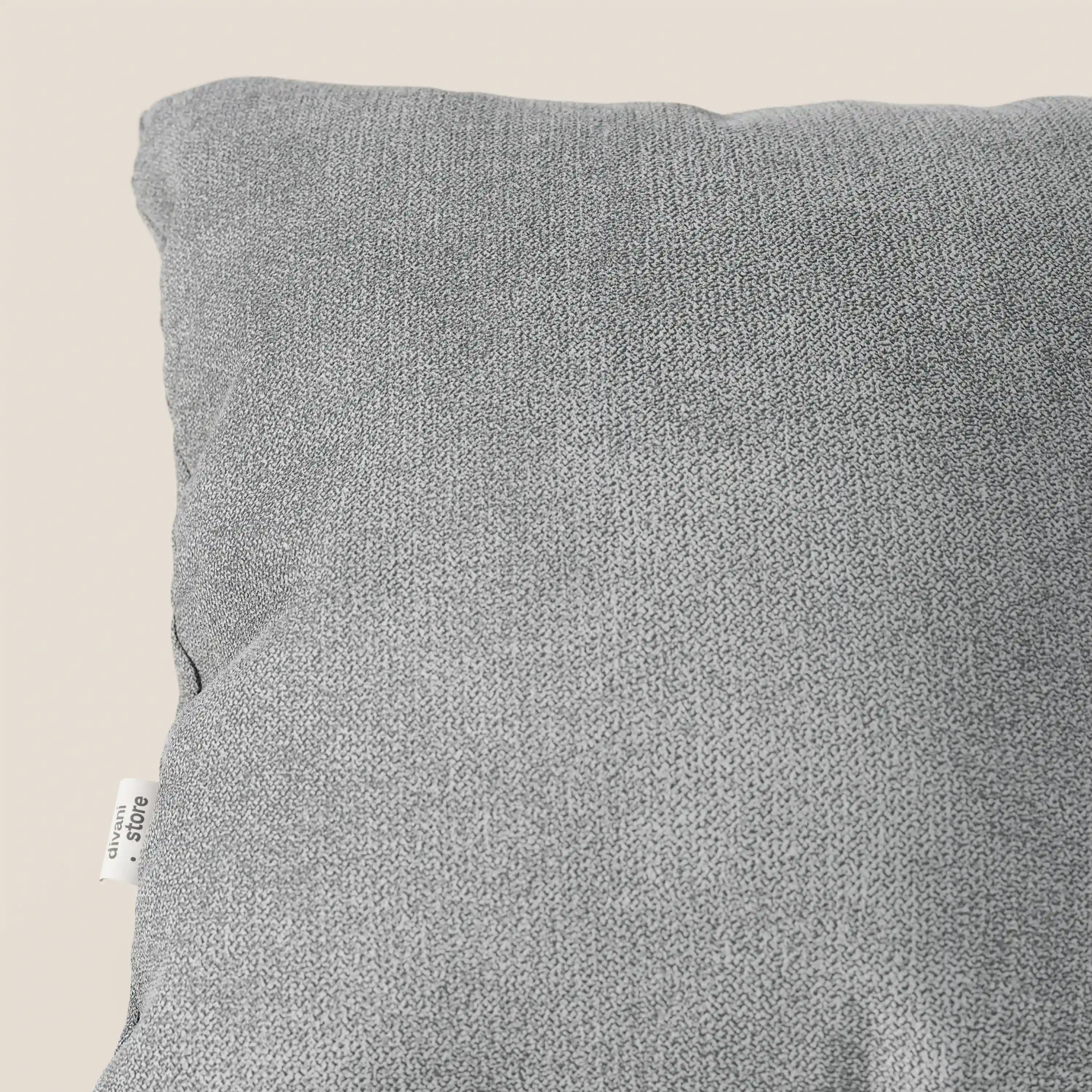 Un primo piano del cuscino lavabile Destiny di Divani.Store in tessuto morbido impermeabile T02 grigio chiaro, 45x45 cm, mostra la sua sottile trama a maglia e l'etichetta in tessuto bianco a sinistra, su uno sfondo beige chiaro.