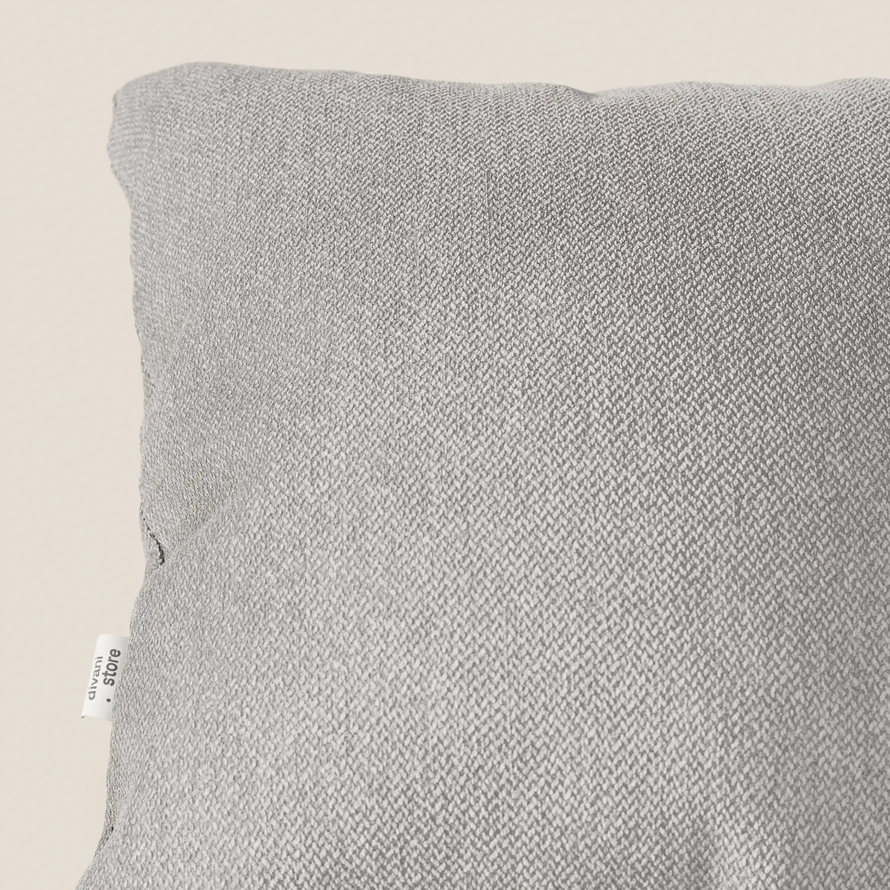 Primo piano dell'angolo superiore sinistro di un cuscino Sogno di Divani.Store in morbido tessuto grigio T05 antimacchia. Una piccola etichetta bianca con testo nero è cucita nella cucitura sinistra; lo sfondo è beige chiaro.