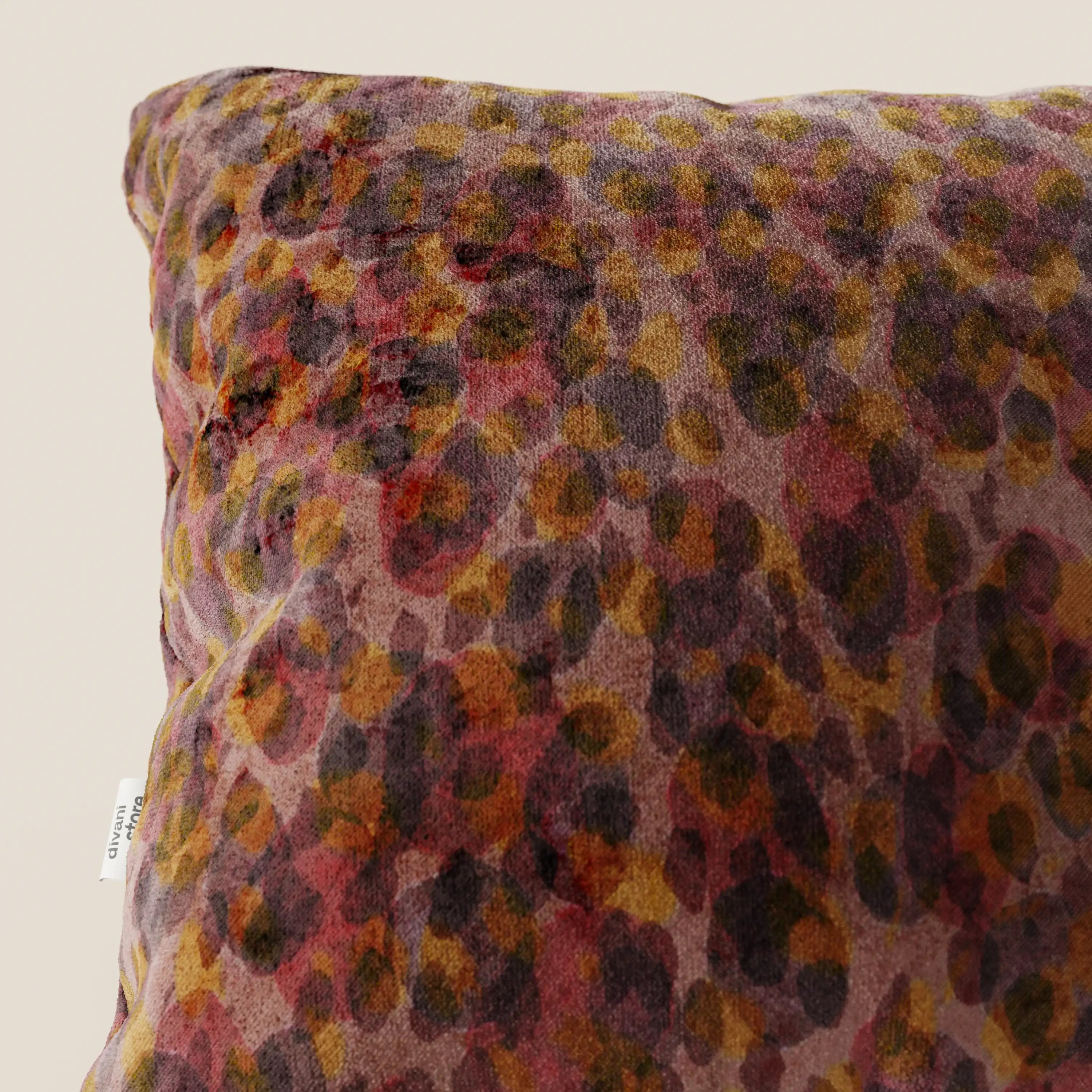 Primo piano di un cuscino Brush 45x45 cm di Divani.Store, realizzato in velluto rosso impermeabile con una stampa leopardata multicolore e una piccola etichetta in tessuto bianco sulla cucitura. Su uno sfondo beige a tinta unita, perfetto per i cuscini decorativi moderni.