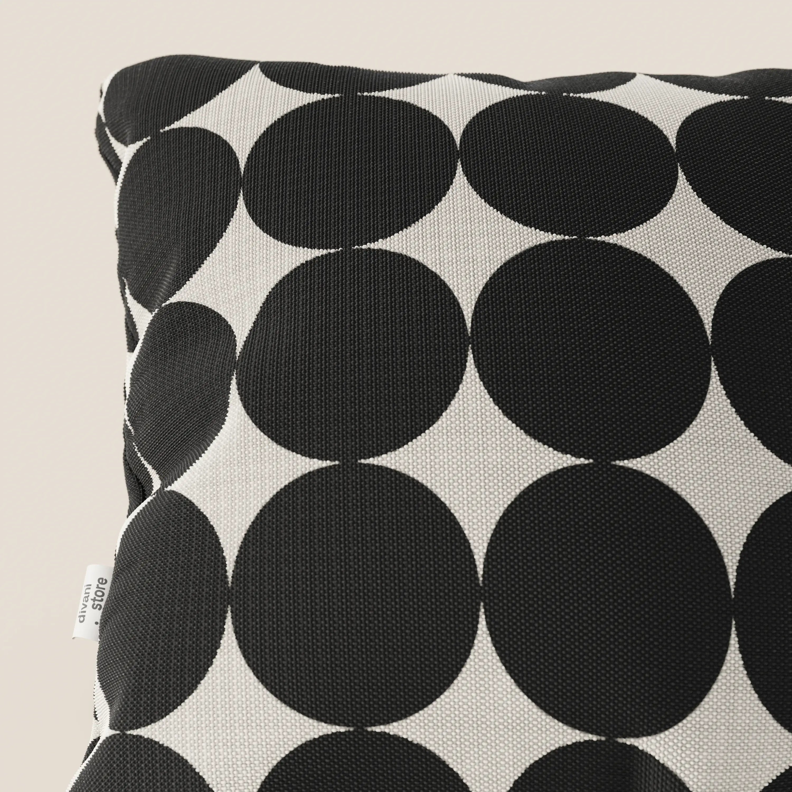Primo piano dei cuscini geometrici Dot di Divani.Store in tessuto idrorepellente nero, caratterizzati da grandi cerchi neri su sfondo bianco. Sul lato compare una piccola etichetta bianca. Il cuscino è inserito in uno sfondo chiaro.