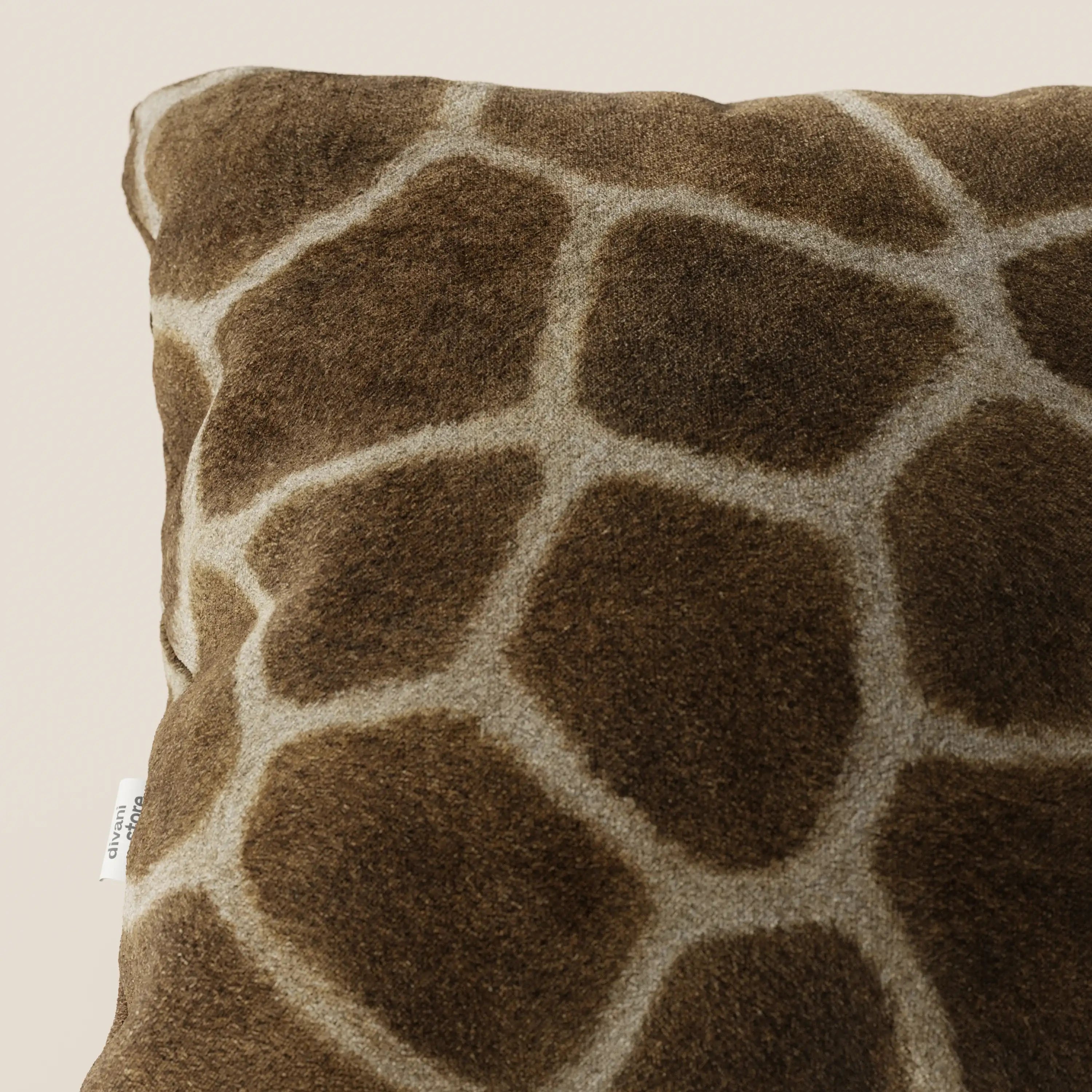 Primo piano del cuscino della collezione Wild in microfibra impermeabile giraffa di Divani.Store, un cuscino quadrato lavabile con rivestimento in morbida ecopelliccia marrone e stampa giraffa color crema, caratterizzato da una piccola etichetta bianca su sfondo beige chiaro.