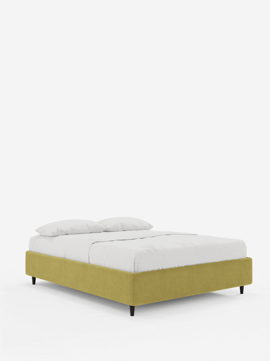 Un moderno letto sommier imbottito ERON con contenitore, rivestito in tessuto impermeabile certificato Oeko-Tex, con base giallo senape e gambe affusolate nere, abbinato a biancheria da letto bianca su uno sfondo grigio chiaro.