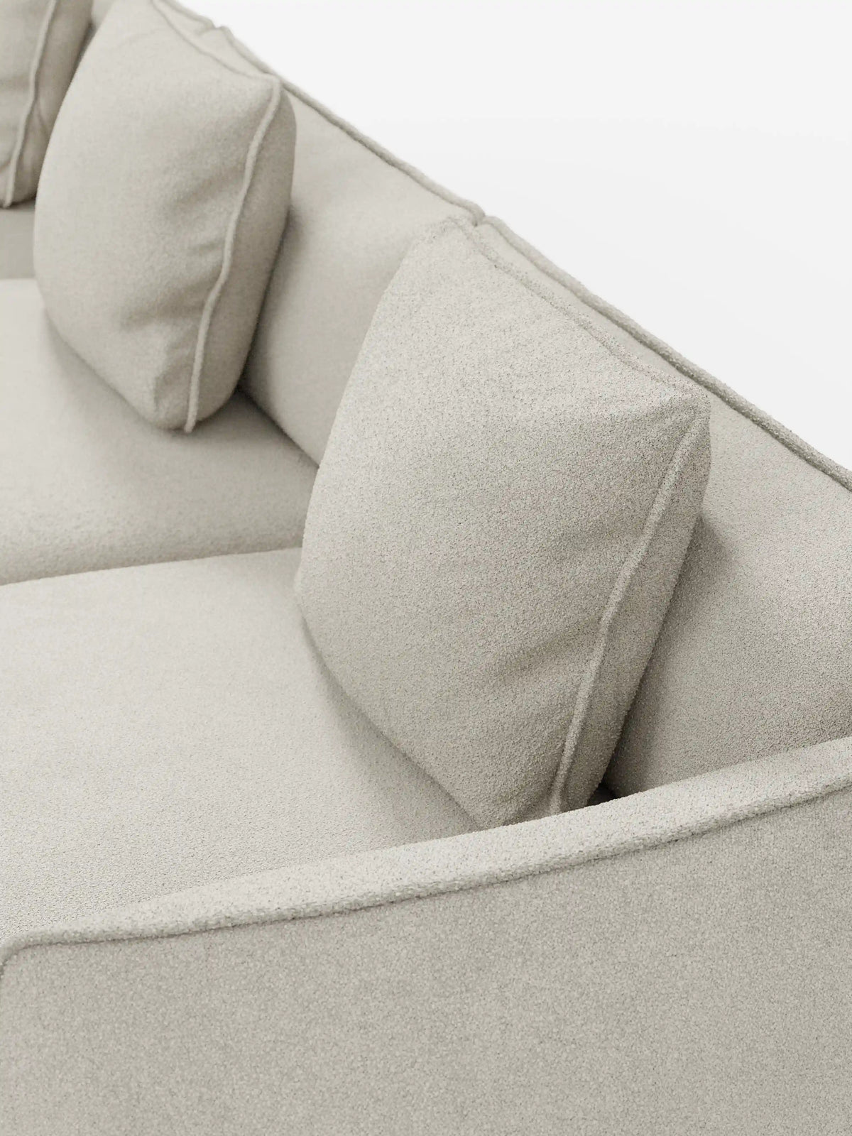 Primo piano del divano modulare a 3 posti “Nimbus” di Divani.Store, rivestito in morbido tessuto T33 effetto cotone, resistente alle macchie, color beige chiaro. Questo divano moderno è caratterizzato da due morbidi cuscini quadrati dello schienale, braccioli imbottiti, linee pulite e un design minimalista. Lo sfondo è bianco a tinta unita.