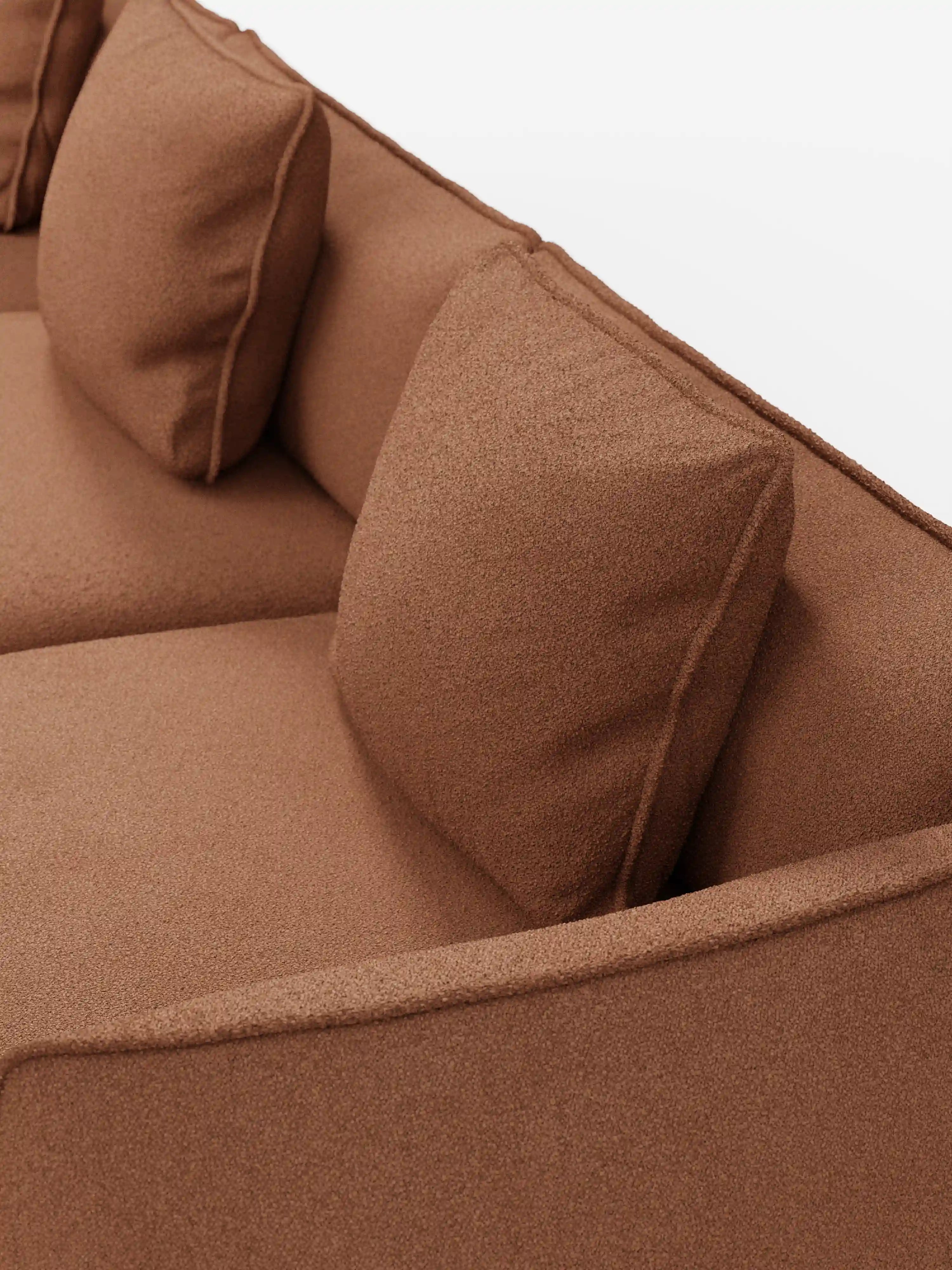 Primo piano del divano modulare a 3 posti “Nimbus” di Divani.Store, rivestito in morbido tessuto T33 effetto cotone, resistente alle macchie, di colore marrone. Il divano modulare presenta linee pulite, braccioli angolati e un design minimalista. Due cuscini quadrati poggiano contro lo schienale, mettendo in risalto l’aspetto leggermente testurizzato del tessuto. Lo sfondo è bianco e a tinta unita.