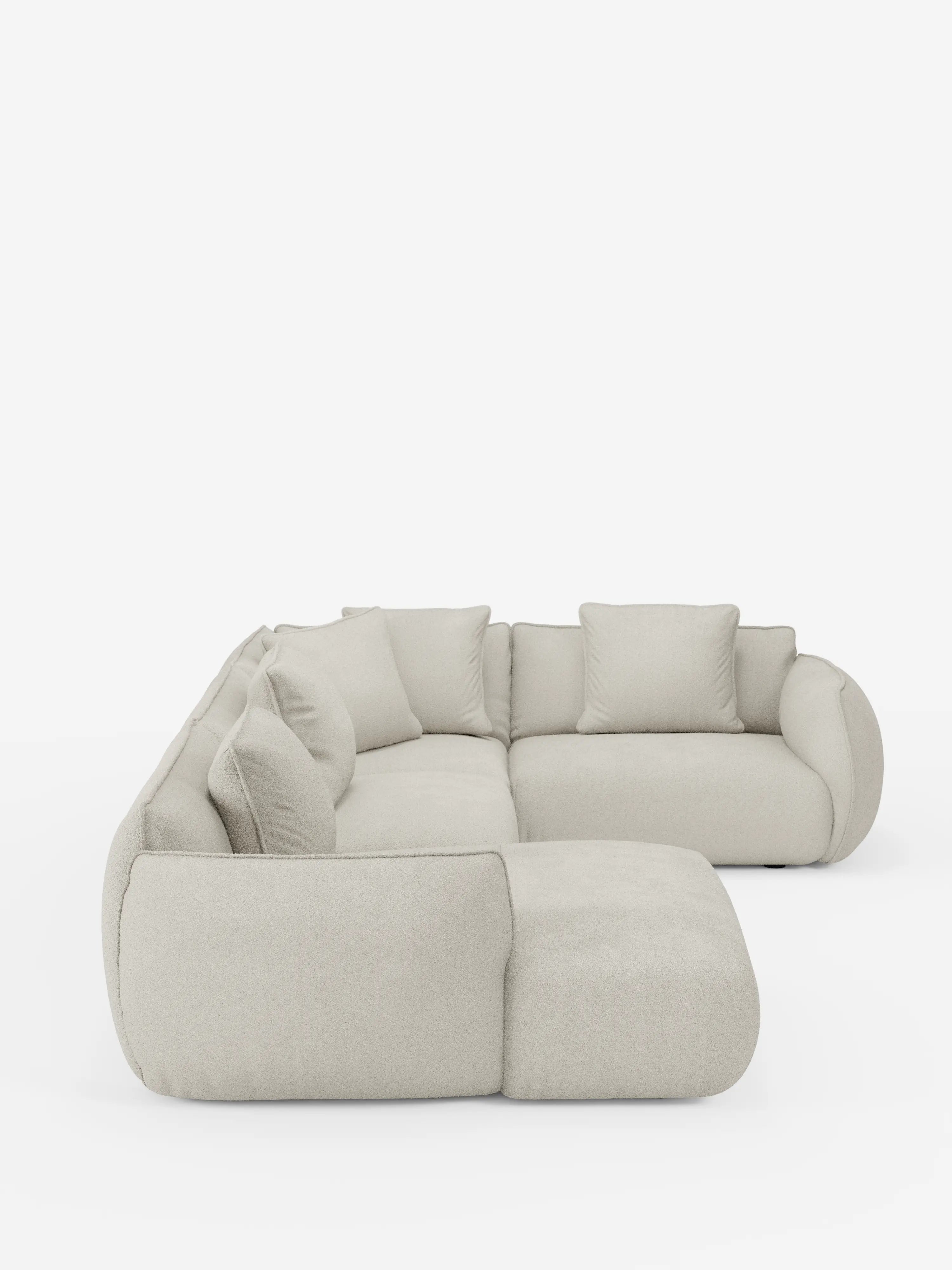 Un moderno divano angolare panoramico componibile Nimbus con penisola e angolo in tessuto smacchiabile T33 di Divani.Store, rivestito in beige chiaro con bordi arrotondati e morbidi cuscini, è esposto su uno sfondo bianco. Il divano a forma di L è composto da cinque sezioni di seduta e sette cuscini schienali coordinati, incarnando un'estetica morbida e contemporanea che mette in risalto la raffinata eleganza dell'artigianato italiano.
