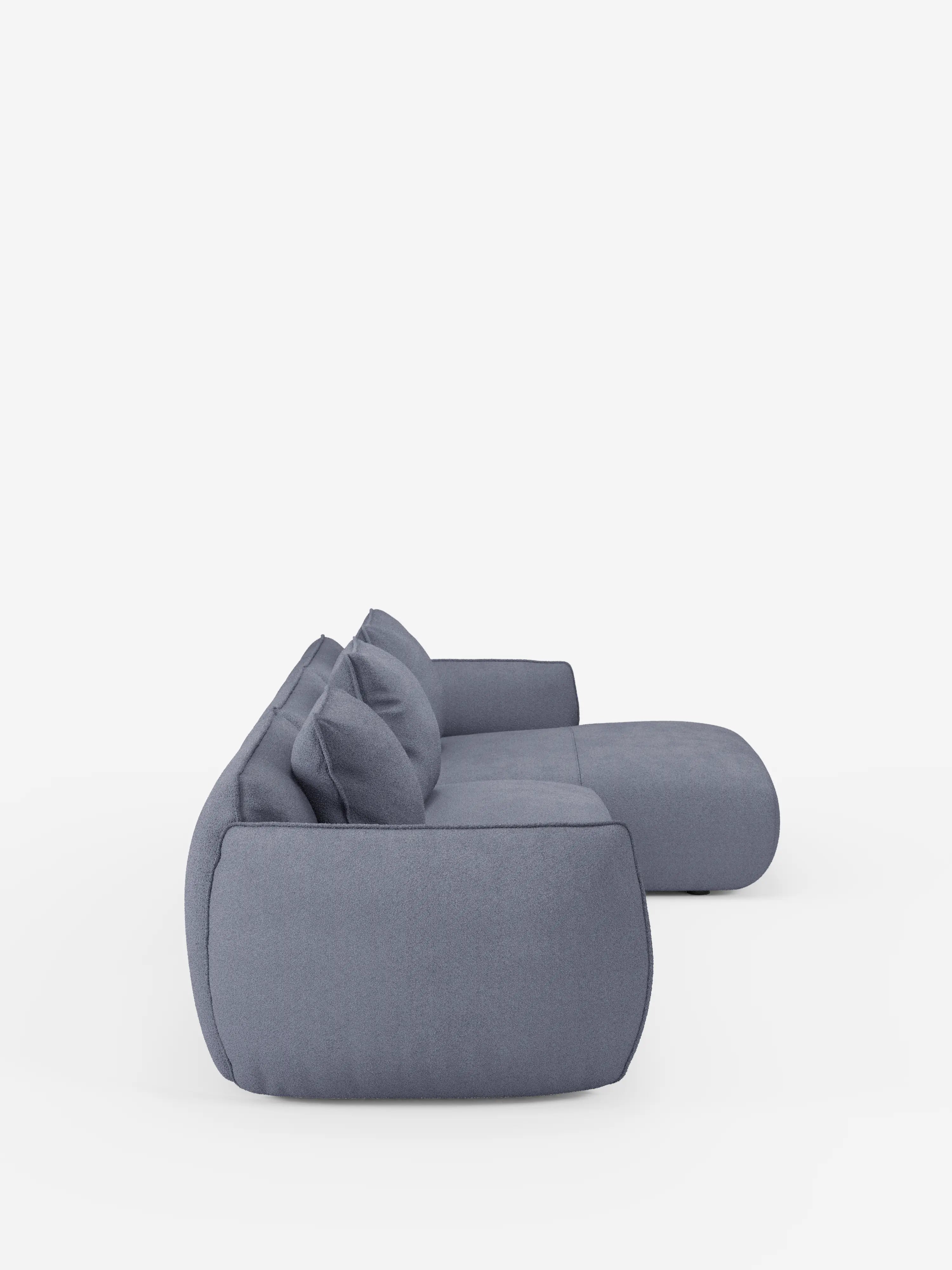 Vista laterale del divano angolare con penisola componibile Nimbus di Divani.Store, rivestito in morbido tessuto T33 effetto cotone, resistente alle macchie, in grigio chiaro. Questo moderno divano componibile presenta cuscini soffici, bordi delicatamente arrotondati e due cuscini dello schienale abbinati, il tutto su uno sfondo bianco a tinta unita. Il design contemporaneo è sobrio e minimalista, e incarna al contempo comfort e stile.