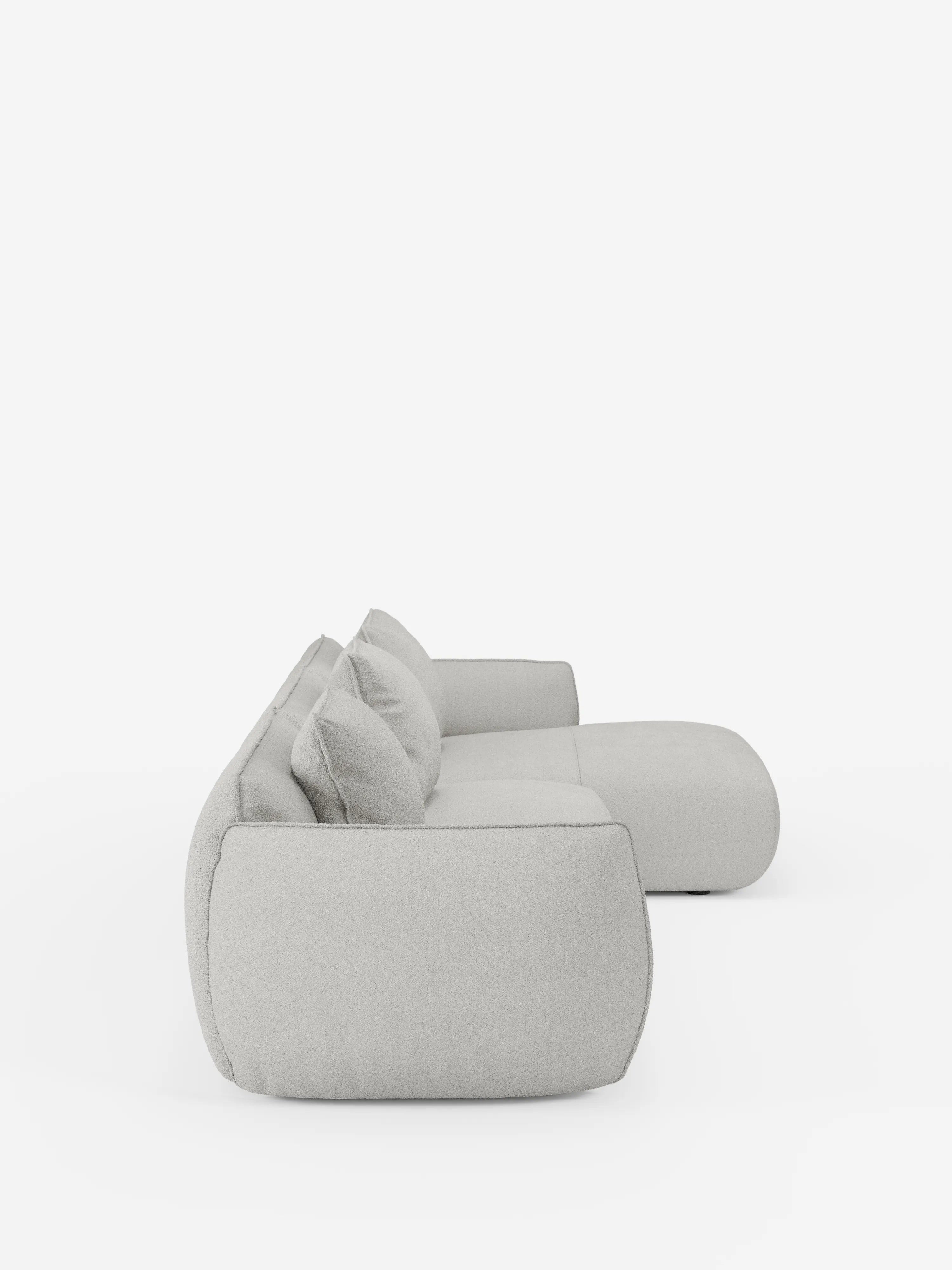 Vista laterale del divano angolare con penisola componibile Nimbus in morbido tessuto effetto cotone smacchiabile T33 di Divani.Store, caratterizzato da un design modulare moderno in grigio chiaro con due grandi cuscini dello schienale e bordi arrotondati, su uno sfondo bianco a tinta unita. Questo divano presenta uno stile minimalista e contemporaneo con un rivestimento morbido e soffice.