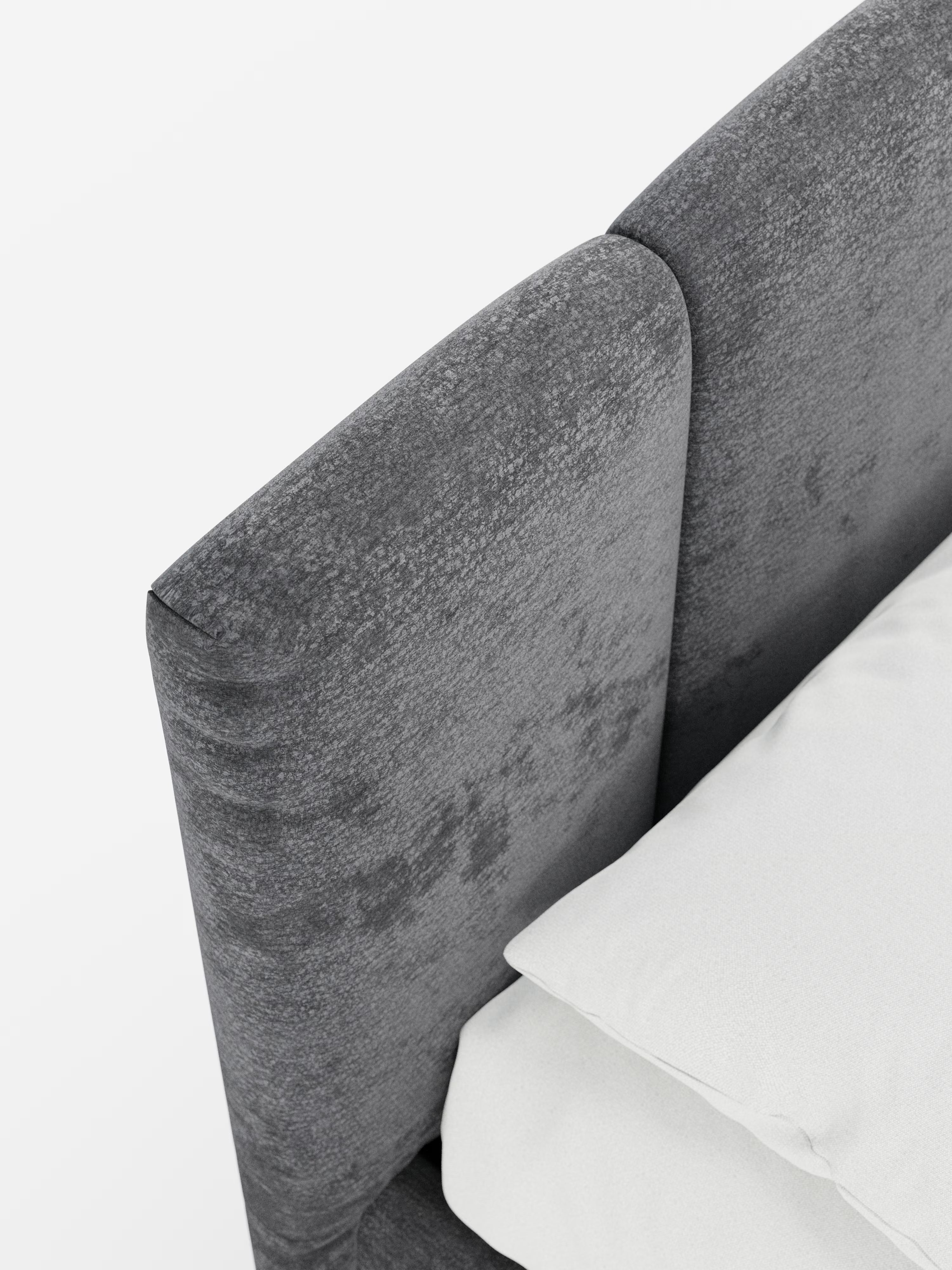 Primo piano in angolazione del letto imbottito ARKAM con vano contenitore e testiera a lavorazione verticale di Letti.Il letto — con una testiera in tessuto grigio certificato Oeko-Tex® caratterizzata da un delicato motivo verticale in stile shabby chic — è posizionato dietro un letto contenitore ben rifatto, con cuscini e biancheria da letto di un bianco candido, il tutto su uno sfondo bianco a tinta unita.