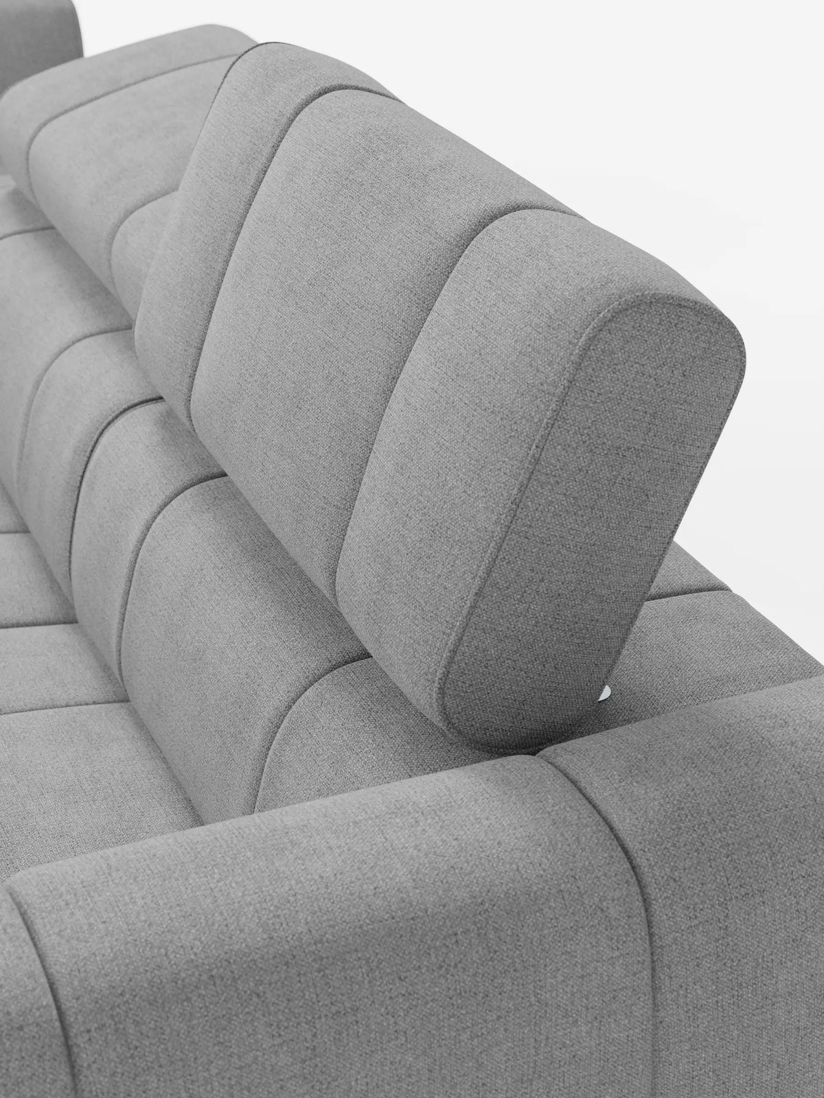 Un divano componibile Giotto Divano grigio chiaro con terminale aperto - opzione relax elettrico in tessuto smacchiabile T23: divano modulare con tessuto testurizzato e poggiatesta imbottiti regolabili, caratterizzati da cuciture verticali su uno sfondo bianco a tinta unita.