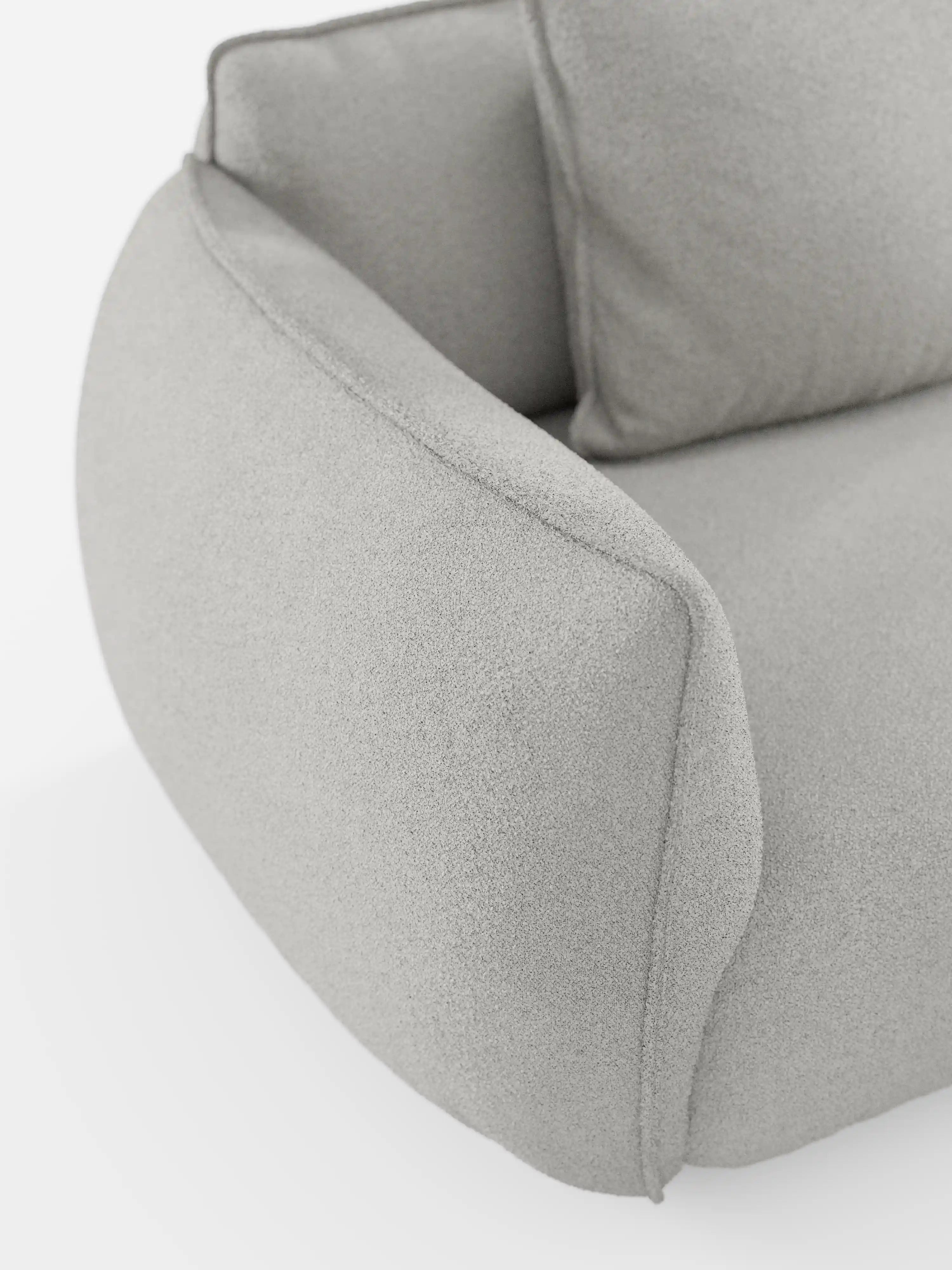 Un primo piano del divano angolare con penisola componibile Nimbus di Divani.Store ne mette in risalto i braccioli e lo schienale, realizzati in tessuto T33 effetto cotone grigio chiaro e resistente alle macchie. Il design moderno è caratterizzato da bordi morbidi e arrotondati e da un'imbottitura soffice, che risaltano sullo sfondo bianco.