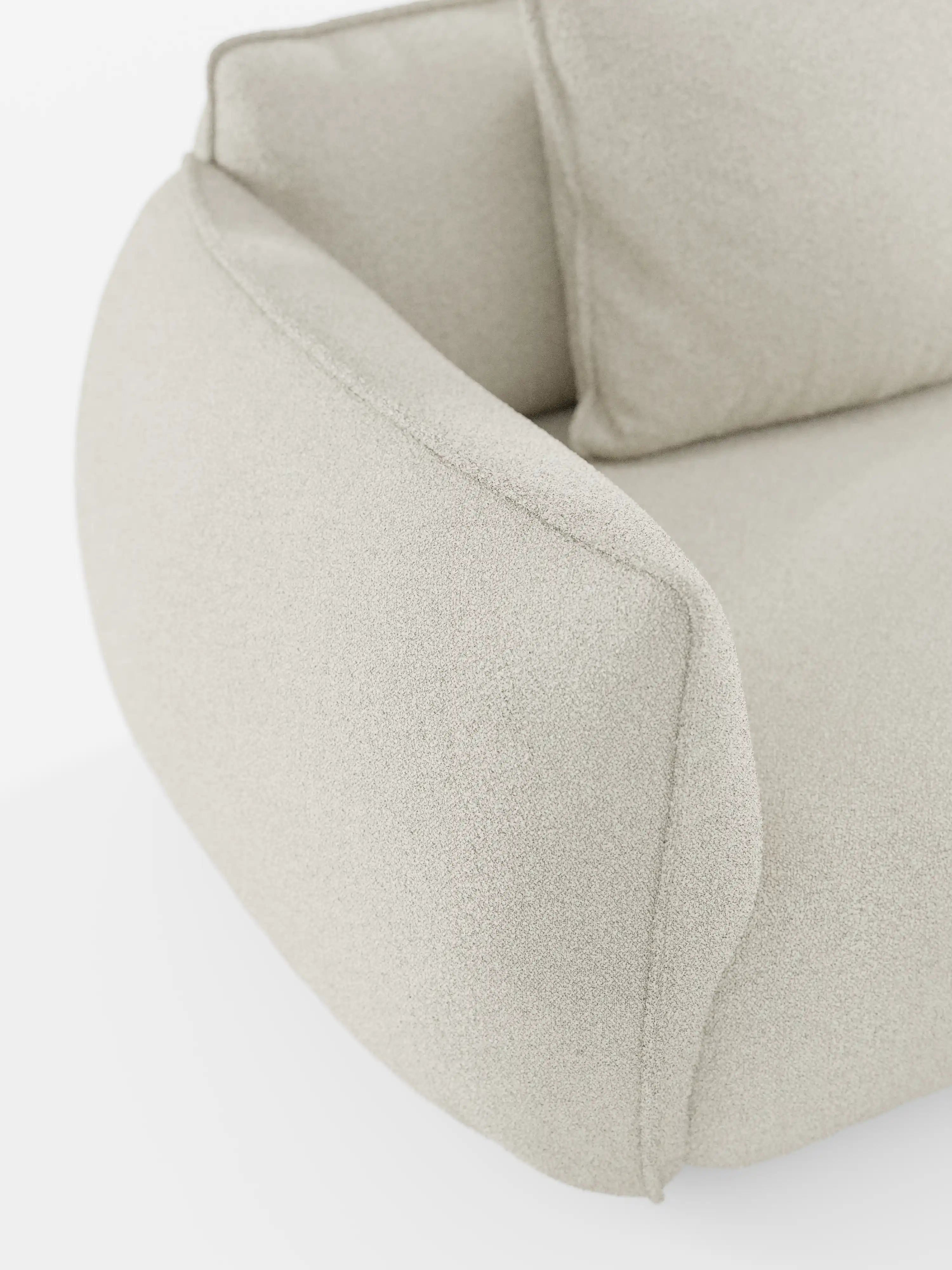 Primo piano del divano angolare con penisola componibile Nimbus di Divani.Store, rivestito in morbido tessuto T33 effetto cotone, resistente alle macchie, in beige chiaro. Questo moderno divano componibile presenta braccioli arrotondati e imbottiti e un cuscino coordinato, che trasmettono comfort e stile su uno sfondo bianco a tinta unita.