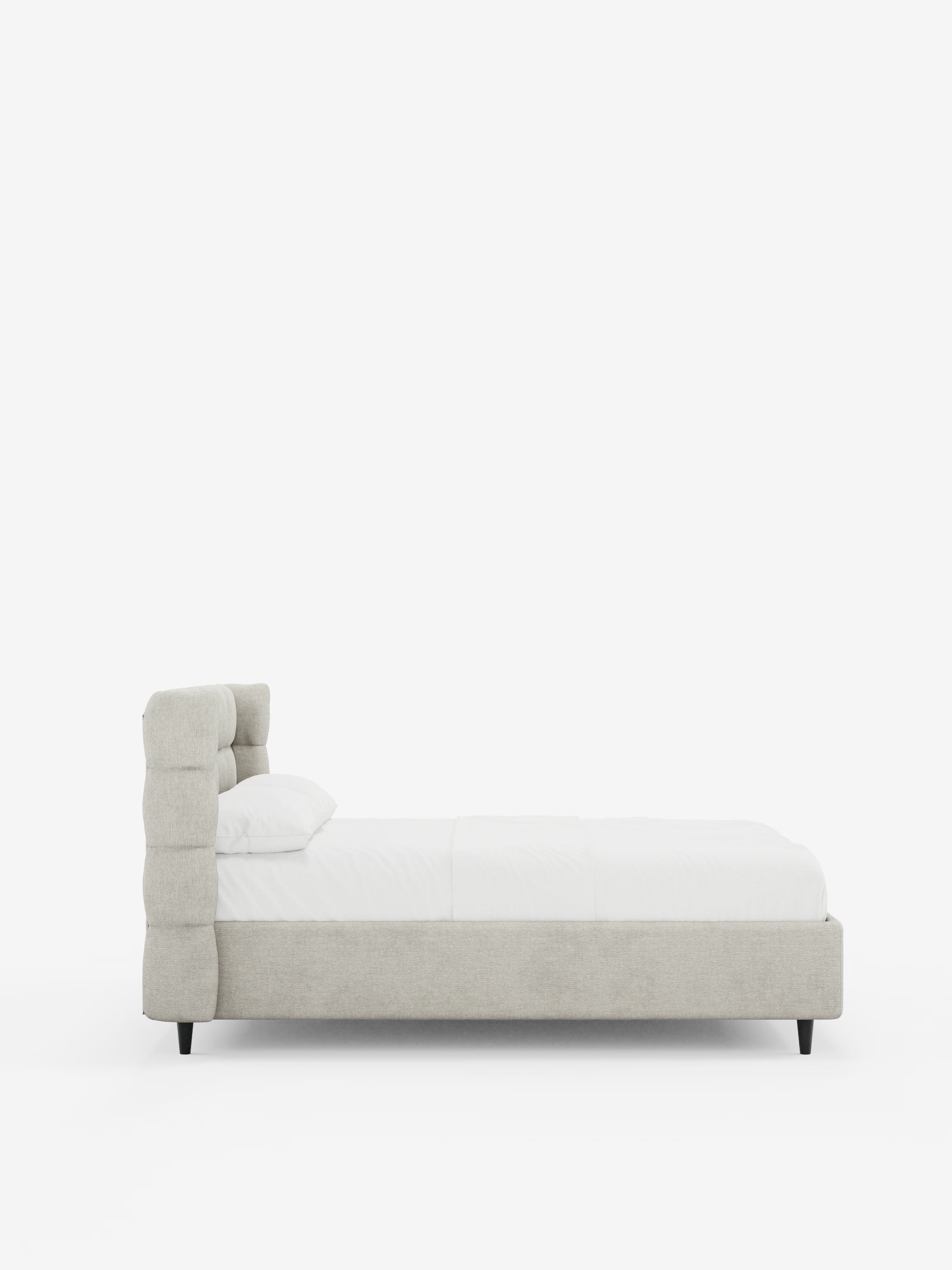Vista laterale del letto imbottito RAGNAR con contenitore e testiera capitonné avvolgente di Letti.store, caratterizzato da un’elegante testiera imbottita in grigio chiaro, certificata Oeko-Tex®, e da una struttura con dettagli capitonné, biancheria da letto bianca e un cuscino singolo. Il letto poggia su corte gambe nere su uno sfondo bianco a tinta unita.