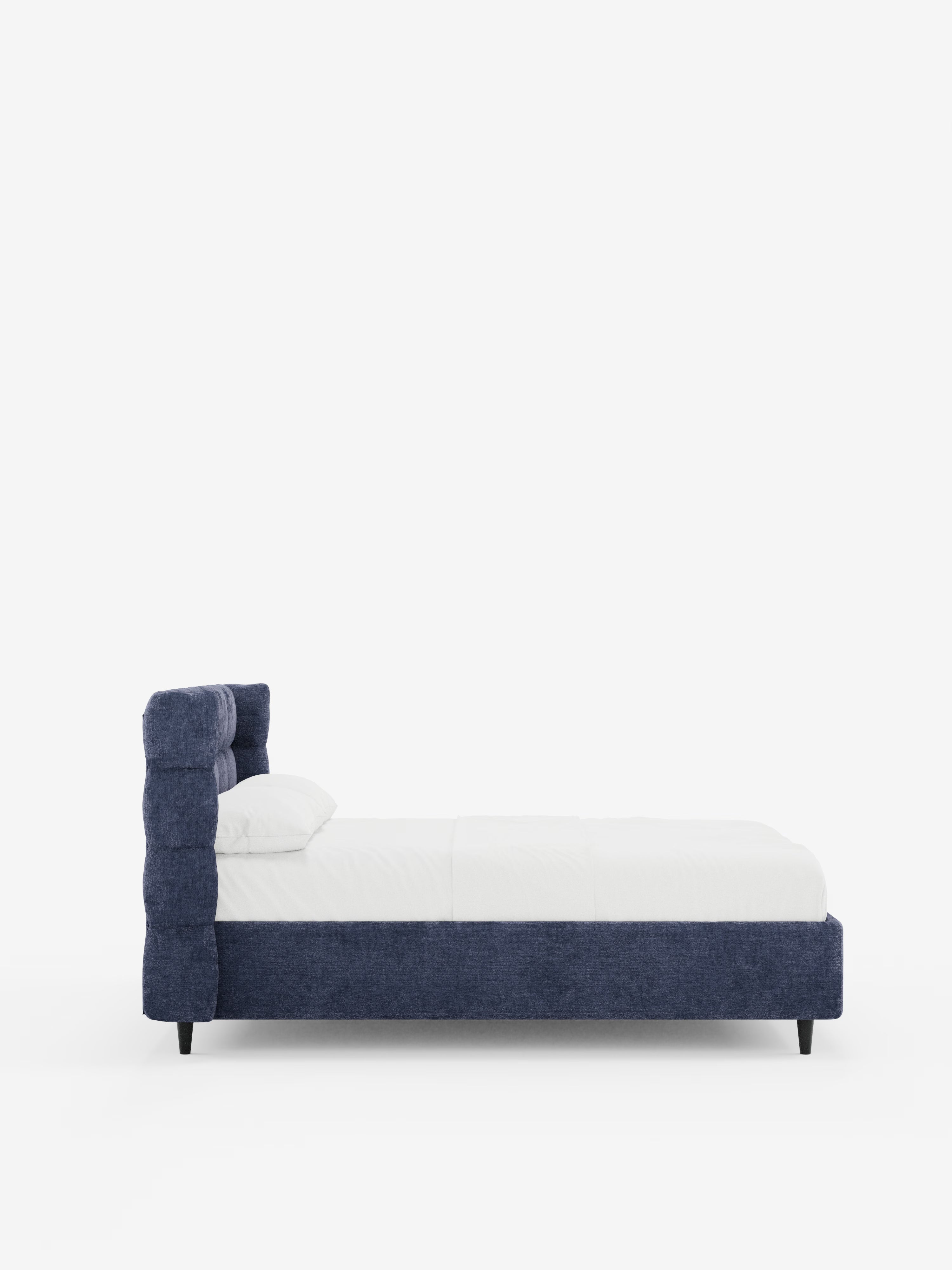 Vista laterale del letto imbottito RAGNAR con contenitore e testiera capitonné avvolgente di Letti.store, caratterizzato da un’elegante testiera blu scuro, capitonné e avvolgente, rivestita in tessuto certificato Oeko-Tex®, biancheria da letto bianca con un unico cuscino e gambe corte di colore scuro. Il design minimalista si staglia su uno sfondo bianco a tinta unita e il letto sembra essere di dimensioni queen o full.