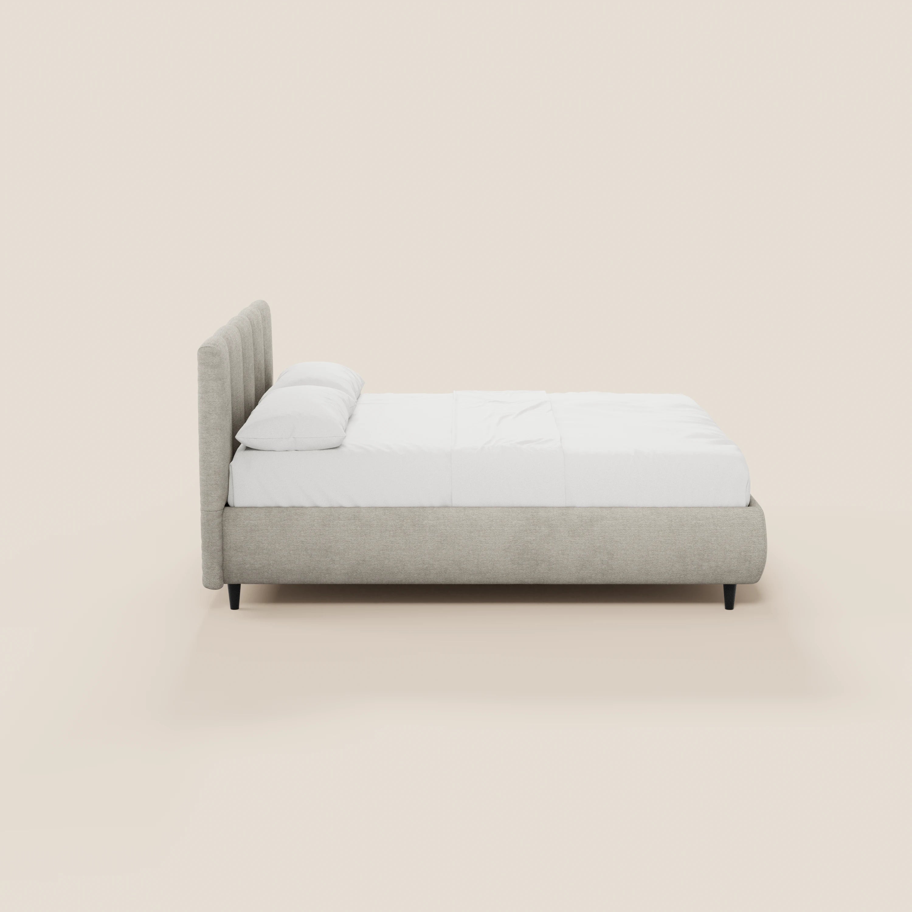 Una vista laterale del letto imbottito ARKAM di Letti.store, caratterizzato da una struttura in tessuto grigio chiaro certificato Oeko-Tex® e da una testiera con cuciture verticali, materasso e cuscini bianchi, gambe corte nere e un design shabby chic su uno sfondo beige a tinta unita.