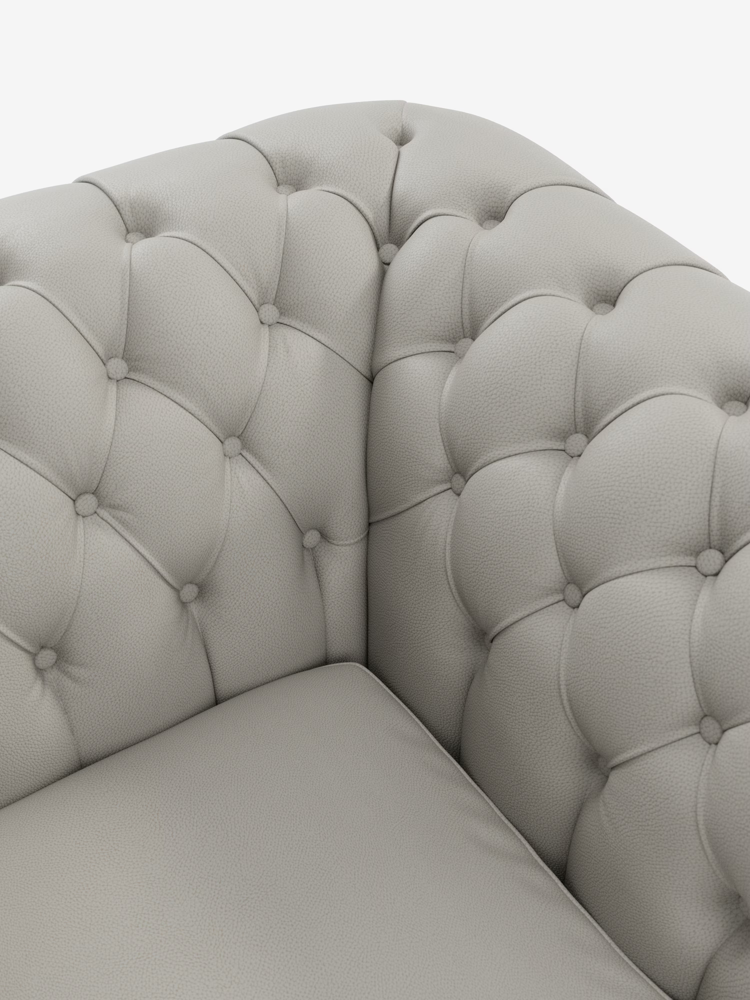 Primo piano della poltrona Chester in vera pelle spessorata con capitonné artigianale di Divani.Store, caratterizzata da un elegante capitonné realizzato a mano e da bottoni decorativi sugli angoli, con un cuscino di seduta liscio, il tutto su uno sfondo bianco.