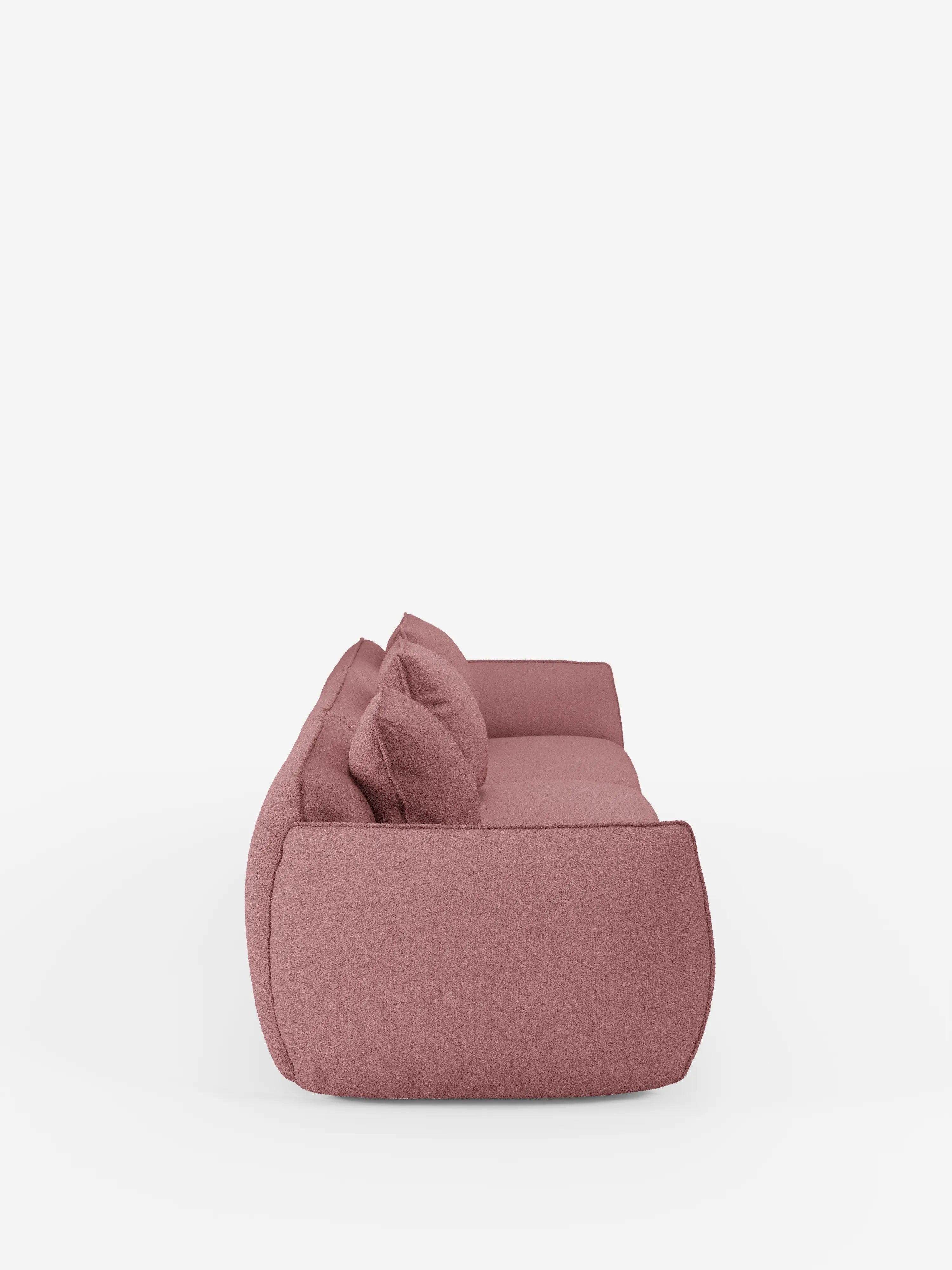 Vista laterale del divano modulare a 3 posti “Nimbus” di Divani.Store, dal design moderno e minimalista, caratterizzato da bordi morbidi e arrotondati e da tre cuscini coordinati in rosa malva. Su uno sfondo bianco, questo divano si distingue per il profilo basso e il rivestimento in tessuto T33 effetto cotone, morbido e resistente alle macchie, che gli conferisce un aspetto accogliente e invitante.