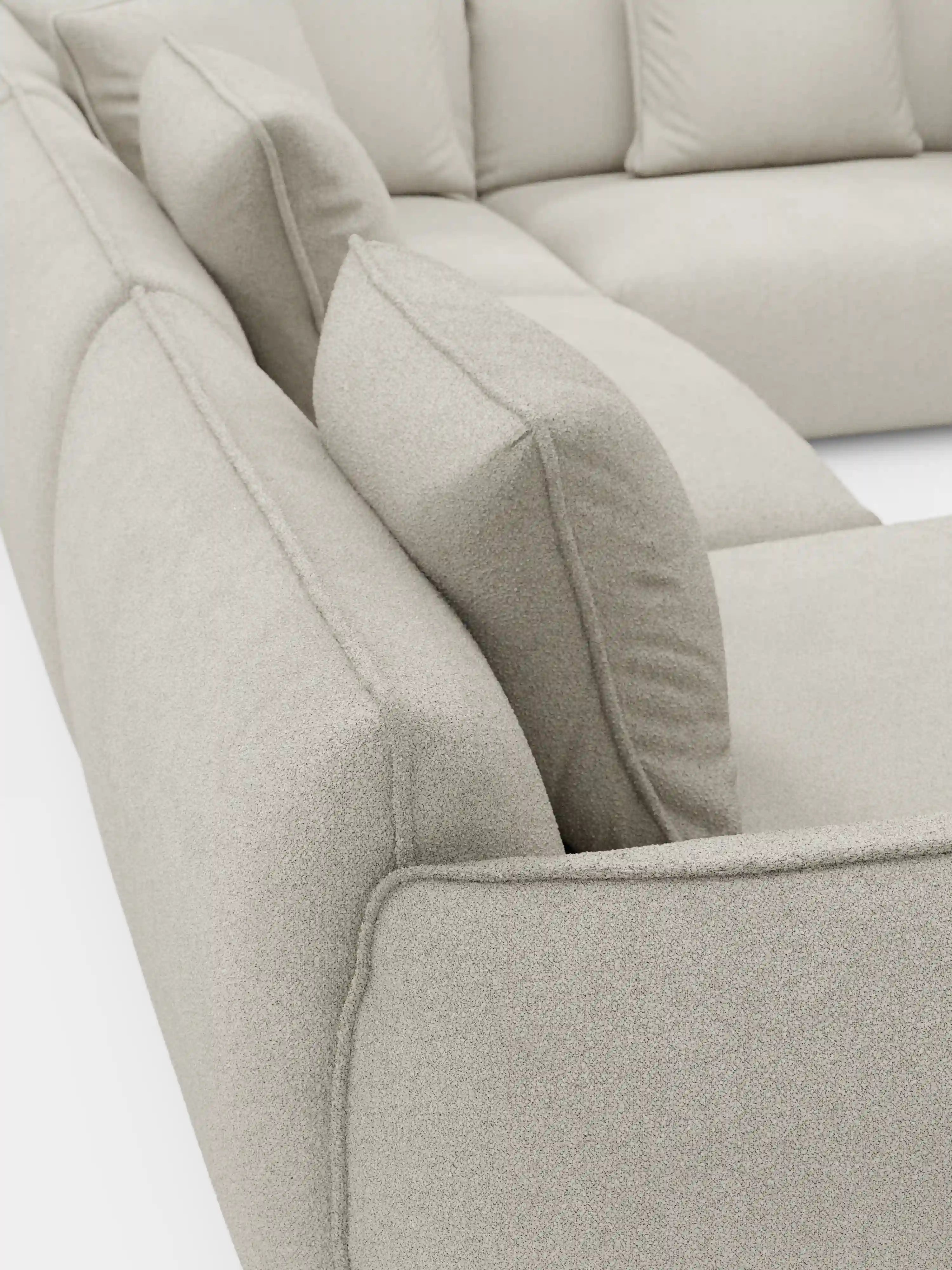 Primo piano del divano angolare panoramico componibile Nimbus con penisola e angolo in tessuto antimacchia T33 di Divani.Store, rivestito in tessuto beige chiaro testurizzato e antimacchia. L'immagine mette in risalto i morbidi cuscini imbottiti e il design pulito e minimalista, con il divano componibile disposto a forma di L su uno sfondo bianco.