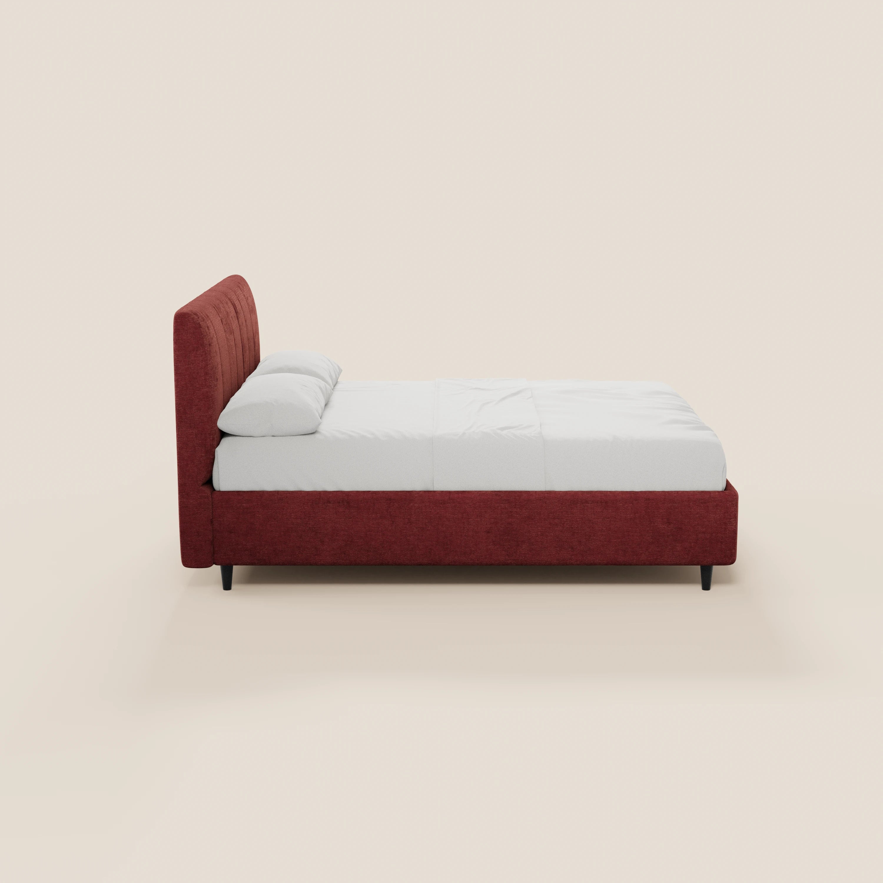 Una vista laterale del letto imbottito ONYX con contenitore e testiera verticale in tessuto Oeko-Tex® di Letti.store, caratterizzato da un'alta testiera rossa, struttura, lenzuola e cuscini bianchi, su quattro corte gambe nere su uno sfondo beige chiaro.