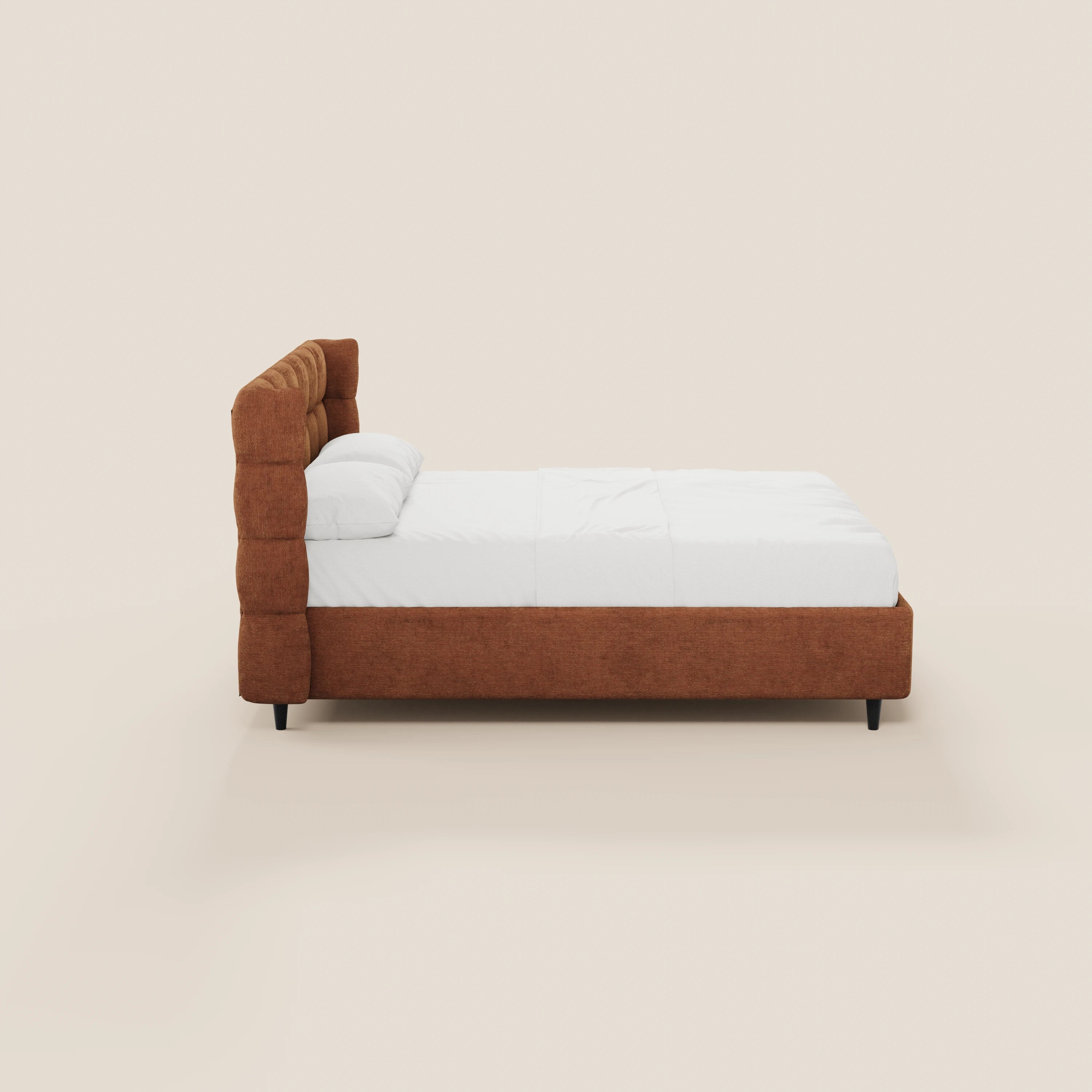 Vista laterale del letto imbottito RAGNAR di Letti.store con testiera avvolgente capitonné color ruggine, biancheria da letto bianca, due cuscini e gambe cilindriche corte nere; il tutto su uno sfondo beige chiaro. Tessuto certificato Oeko-Tex®.