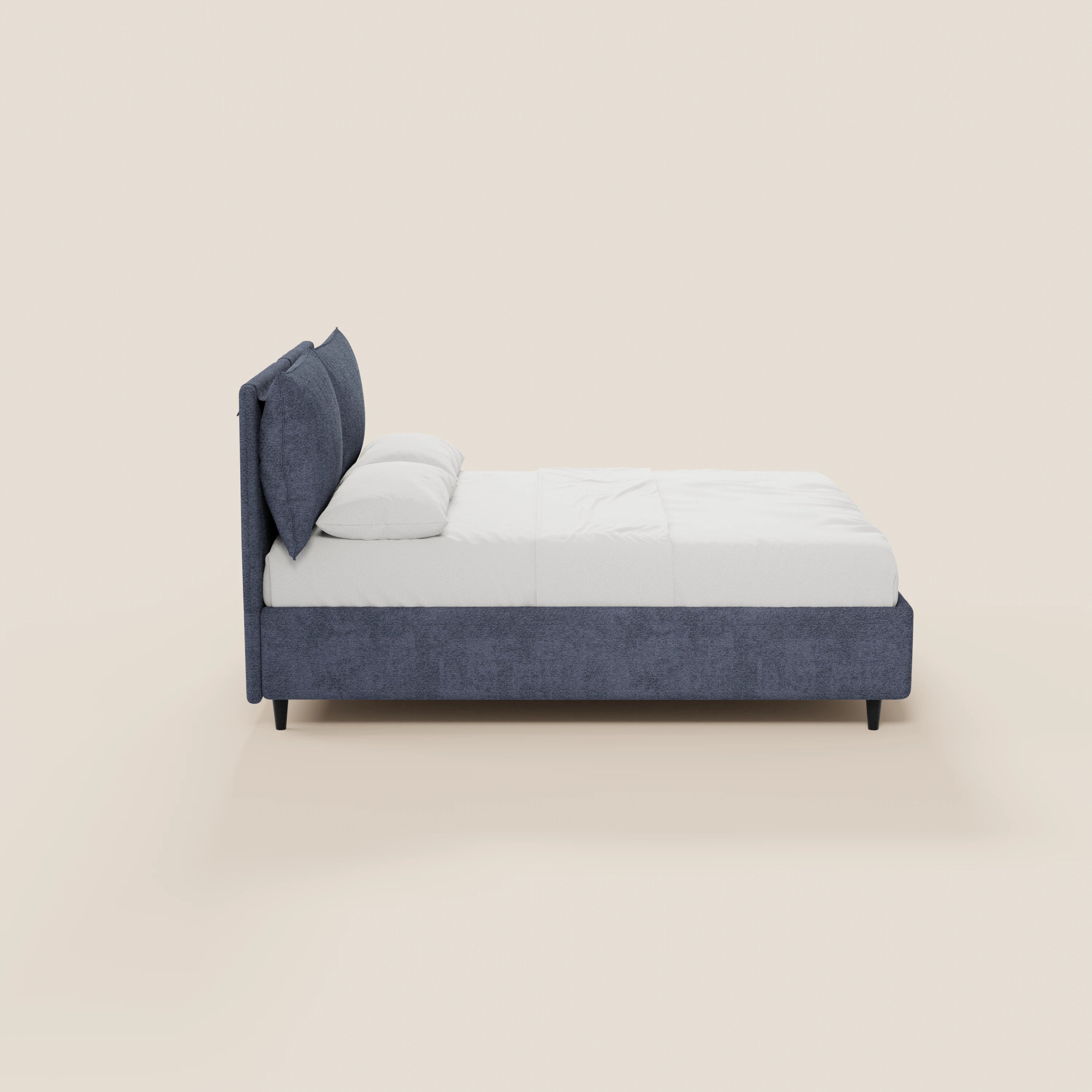 Una vista laterale del letto imbottito ZAYRON di Letti.store con contenitore, in stile moderno e rivestito in tessuto Oeko-Tex®, con testiera regolabile, morbidi cuscini, biancheria da letto bianca e due cuscini appoggiati su quattro gambe nere, su uno sfondo beige chiaro.
