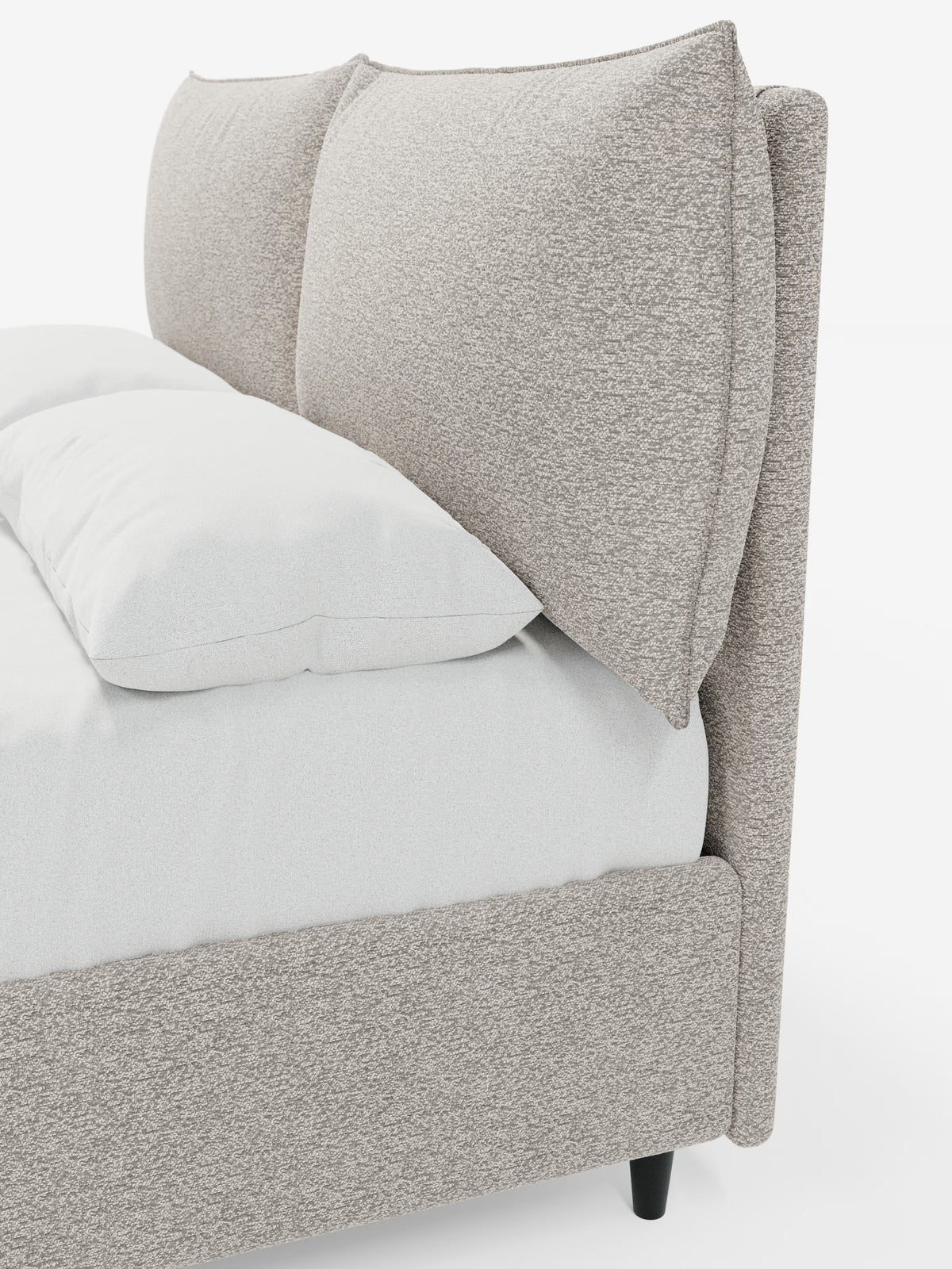 Un primo piano del letto imbottito ZAYRON con contenitore e morbidi cuscini regolabili di Letti.store ne mette in risalto il design moderno, caratterizzato da una struttura in tessuto beige testurizzato certificato Oeko-Tex® e da una testiera oversize, morbida e regolabile, in stile cuscino. Il letto è rivestito con biancheria da letto bianca e poggia su gambe corte nere, su uno sfondo bianco a tinta unita.