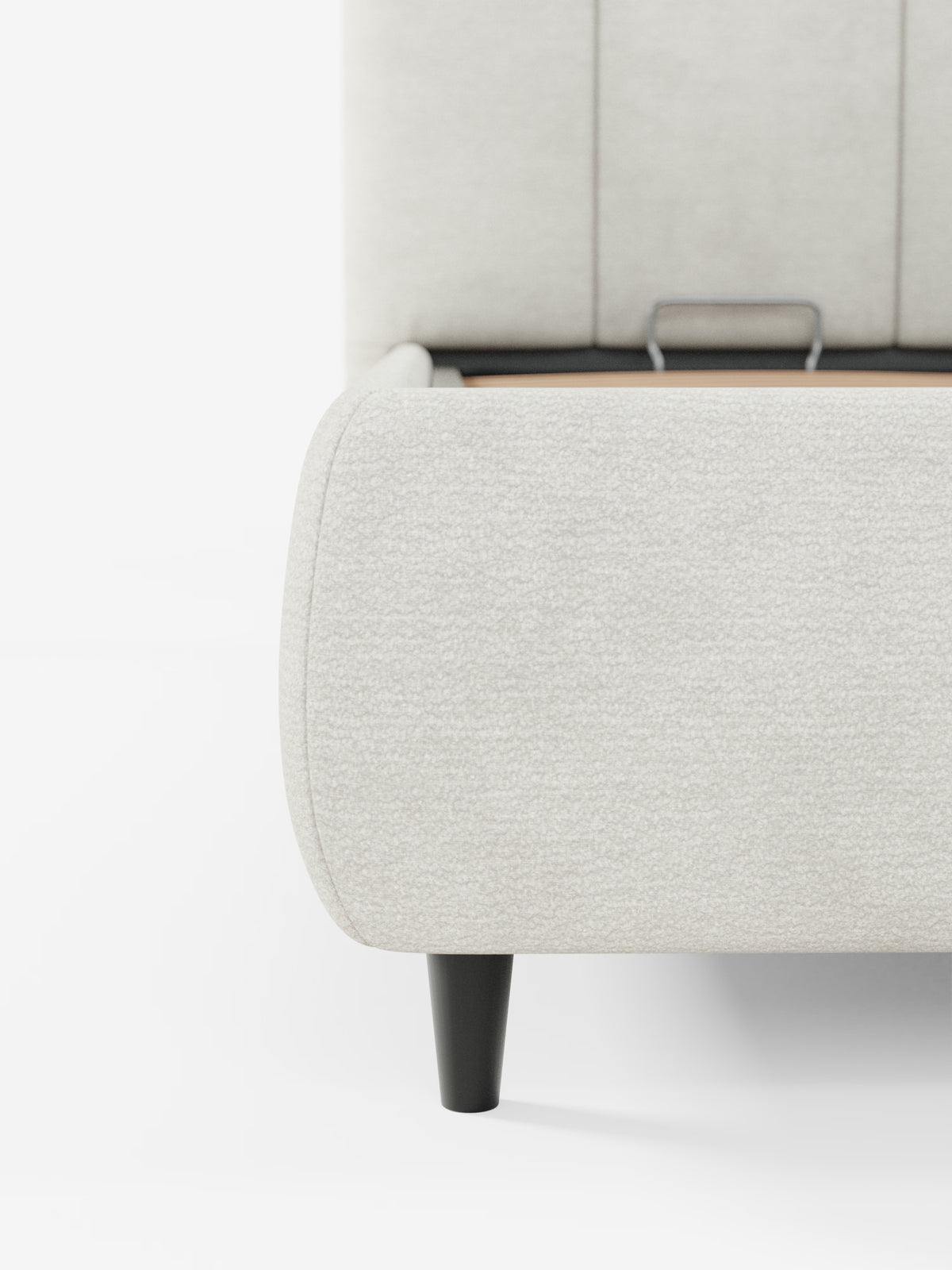 Primo piano del letto imbottito ARKAM con contenitore e testiera a lavorazione verticale di Letti.store, presentato in tessuto bianco sporco certificato Oeko-Tex®. L’immagine mette in risalto la texture delicata del letto, i bordi arrotondati e l’alta testiera imbottita con cuciture verticali, con una gamba cilindrica nera e una parte del supporto metallico interno visibile. Sia lo sfondo che il pavimento sono di un bianco brillante.