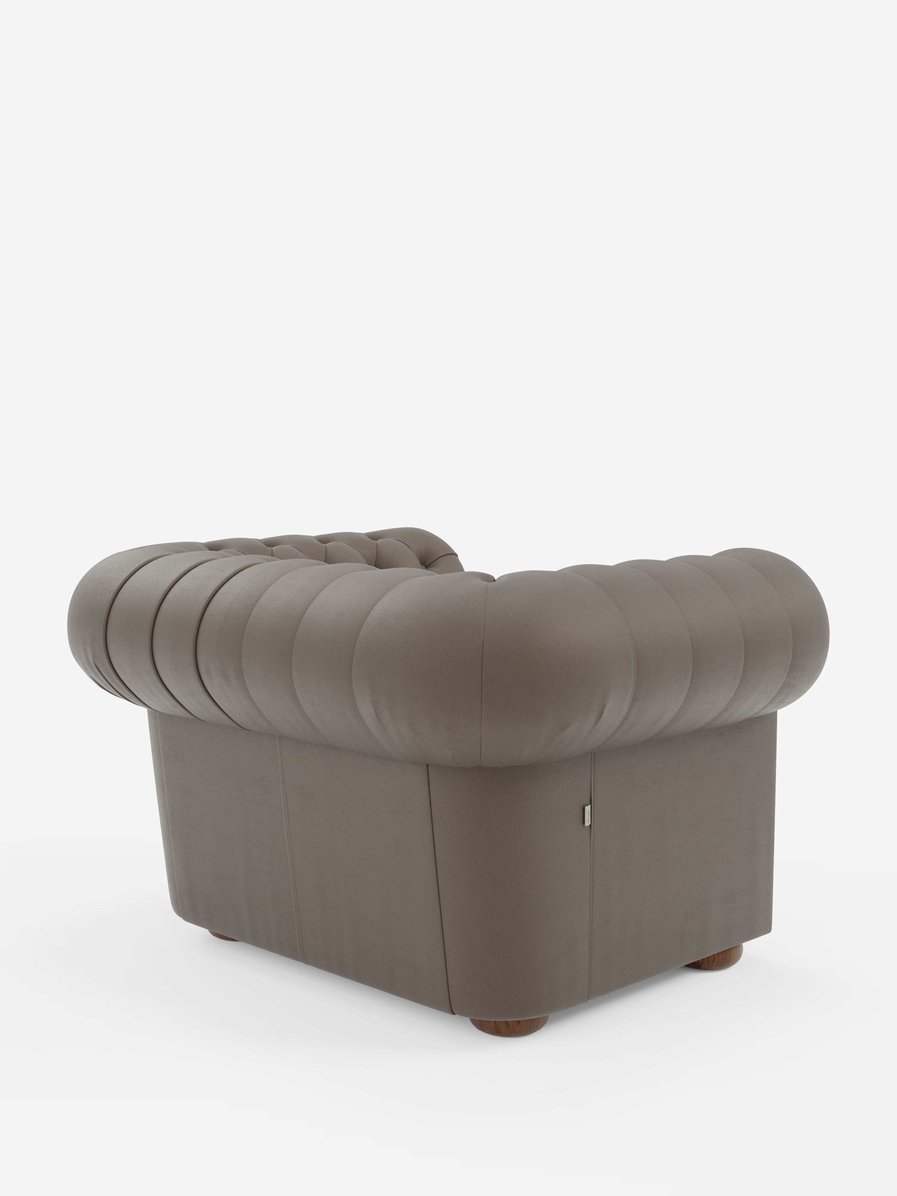 Una poltrona Chester lussuosa e contemporanea di Divani.Store, realizzata in pelle vera di grosso spessore con rifiniture capitonné di fattura artigianale. Questa poltrona presenta uno schienale e braccioli arrotondati e trapuntati, morbide linee curve e una base squadrata e robusta con piedini bassi in legno. Nella foto è raffigurata rivestita in pelle color taupe su uno sfondo bianco a tinta unita.