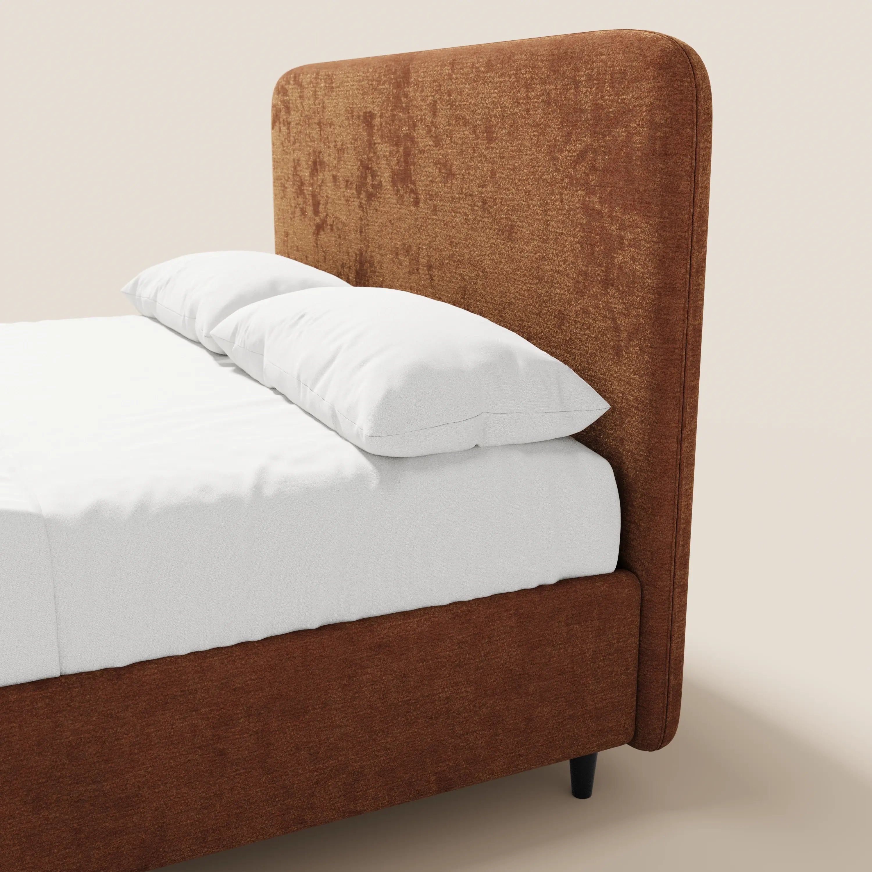 Un primo piano del letto KAELOS minimal imbottito di Letti.store, con testiera e struttura alte in ciniglia color ruggine, lenzuolo con angoli bianco e due cuscini bianchi, appoggiato su gambe alte scure su uno sfondo beige chiaro a tinta unita.