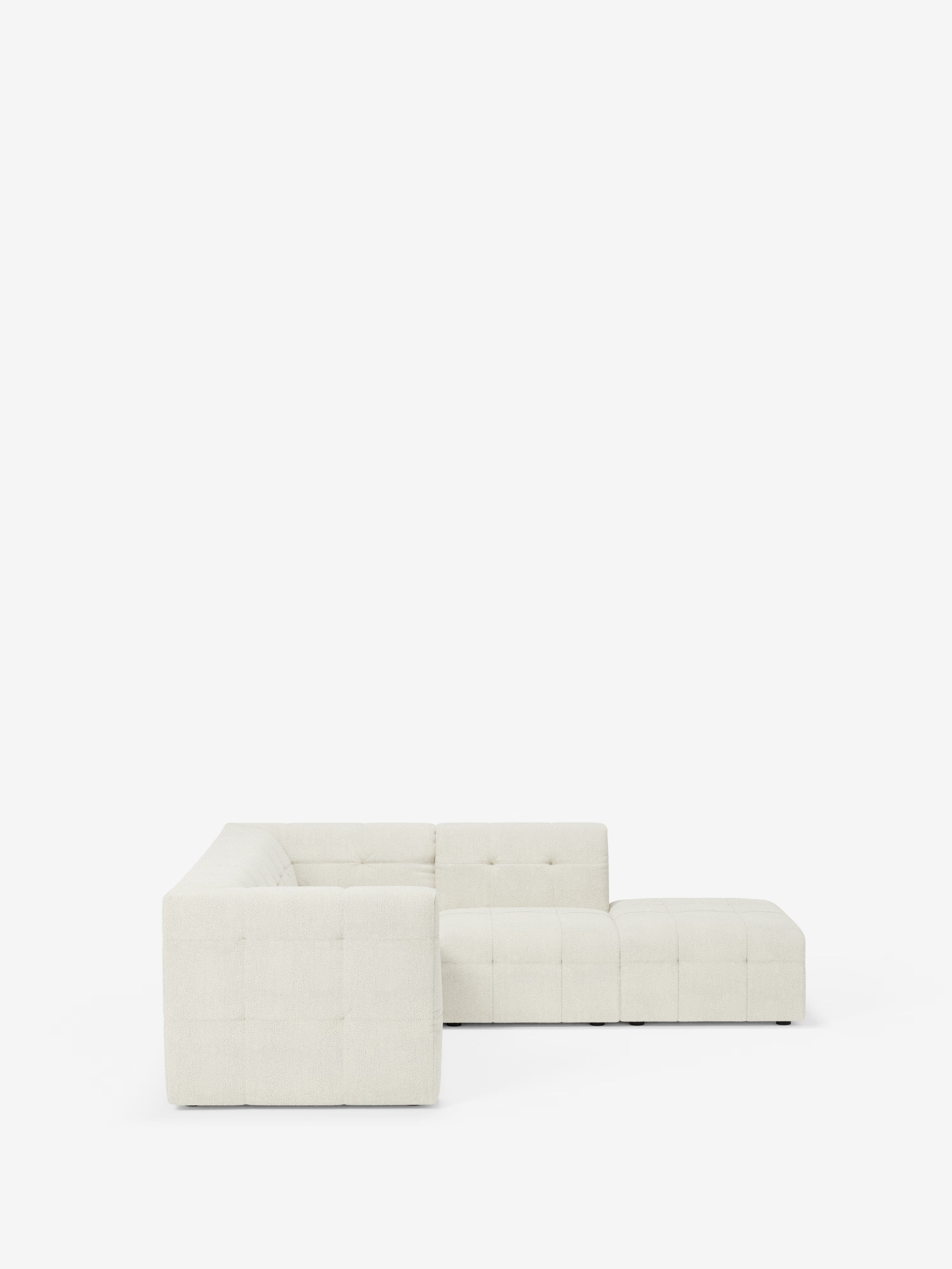 Un divano angolare componibile e modulare della linea Mosaic in bouclé T21 di Divani.Store, con cuscini capitonné e braccioli bassi e larghi in tessuto beige chiaro antimacchia, spicca su uno sfondo bianco a tinta unita: un elemento centrale ideale per qualsiasi soggiorno moderno.