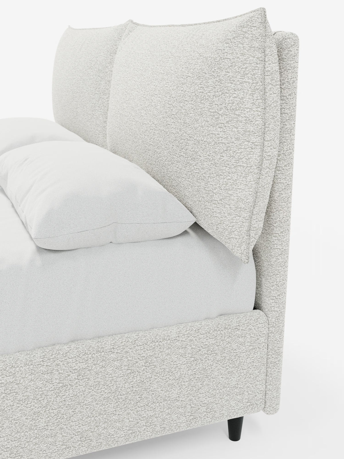 Un primo piano del letto imbottito ZAYRON con contenitore e morbidi cuscini regolabili di Letti.store, caratterizzato da un design moderno in tessuto grigio chiaro testurizzato certificato Oeko-Tex®. Il letto presenta due grandi cuscini morbidi e regolabili che fungono da testiera e una biancheria da letto di un bianco candido. È inclinato in modo da mostrare sia il lato che una parte della parte anteriore, con brevi gambe nere visibili sotto la struttura imbottita.