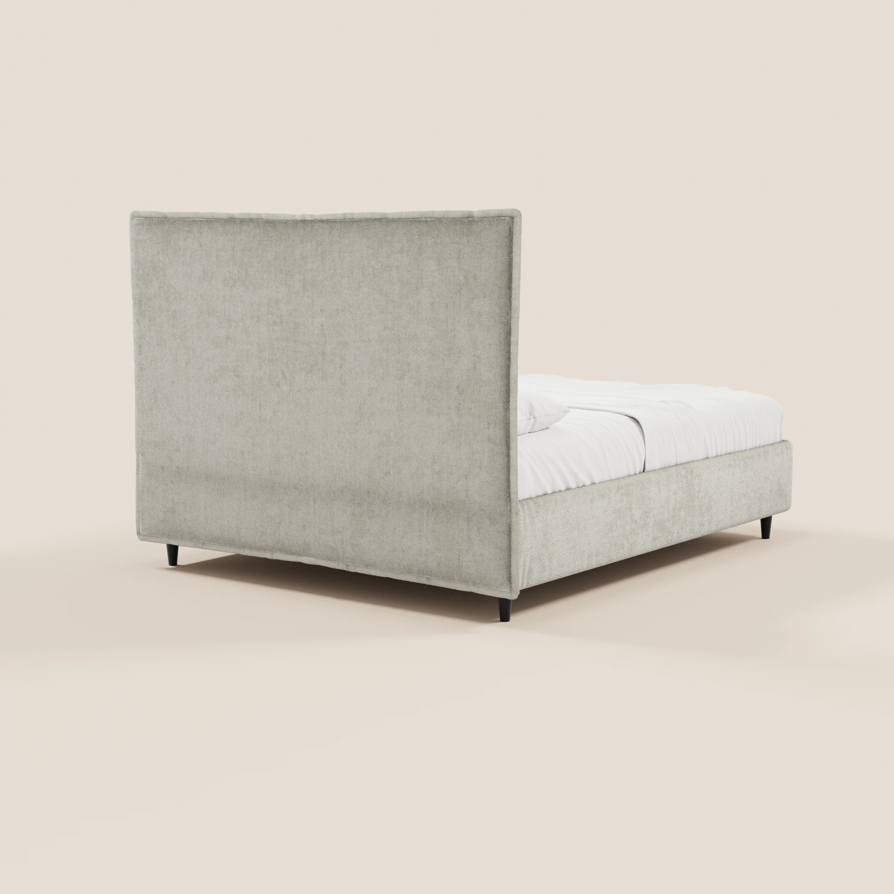 Il letto imbottito AURO con contenitore di Letti.store presenta una testiera capitonné alta in ciniglia Oeko-Tex® grigio chiaro, gambe nere corte e biancheria da letto bianca, ripreso in un’immagine che ne mostra un angolo laterale su uno sfondo beige chiaro.