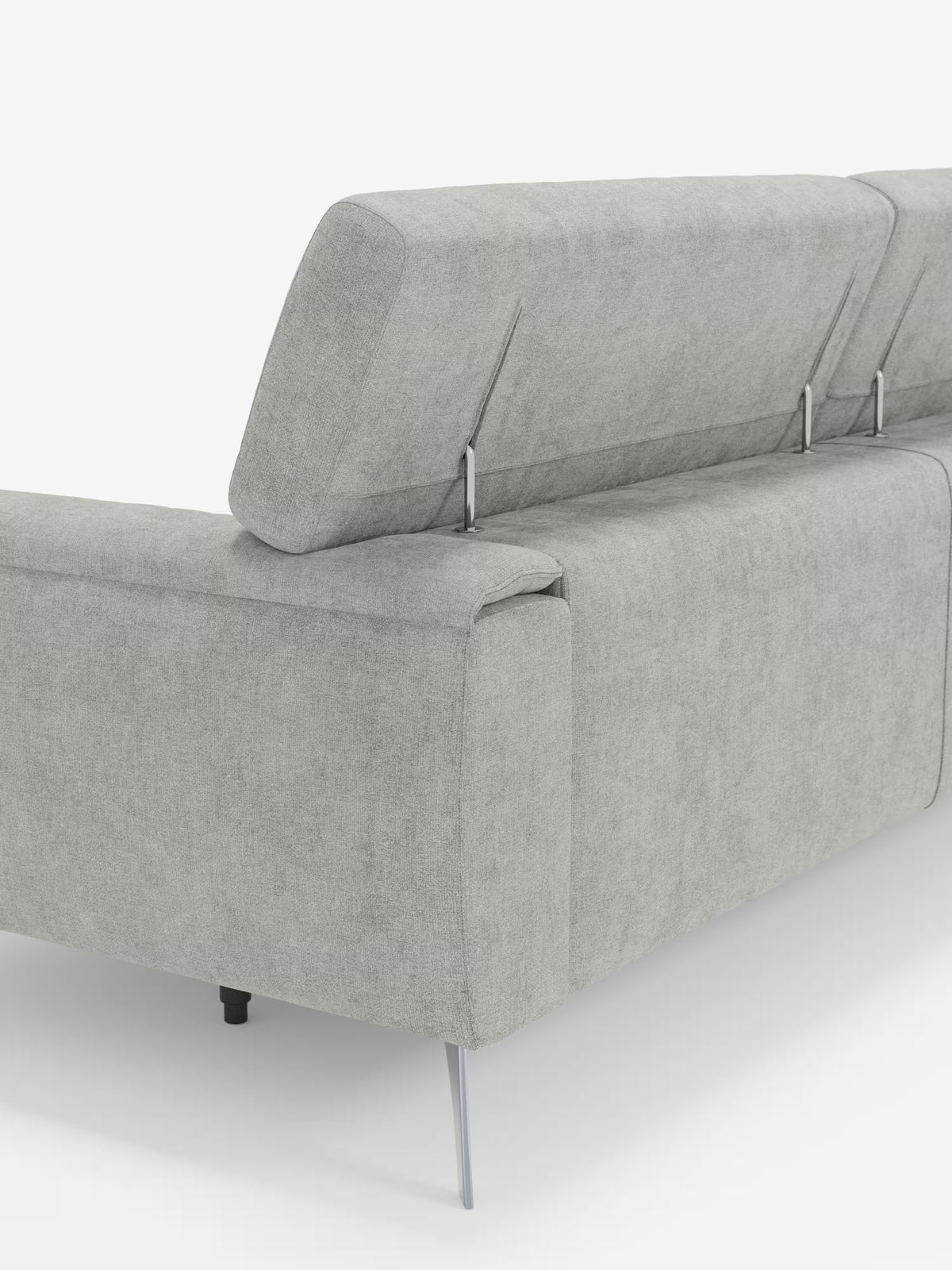 Un divano Caravaggio contemporaneo a 2 e 3 posti di colore grigio chiaro, realizzato da Divani.Store e rivestito con l'elegante tessuto antimacchia T31, è raffigurato nella vista posteriore sinistra. Il divano presenta poggiatesta regolabili con supporti in metallo e raffinate gambe in metallo, su uno sfondo bianco.