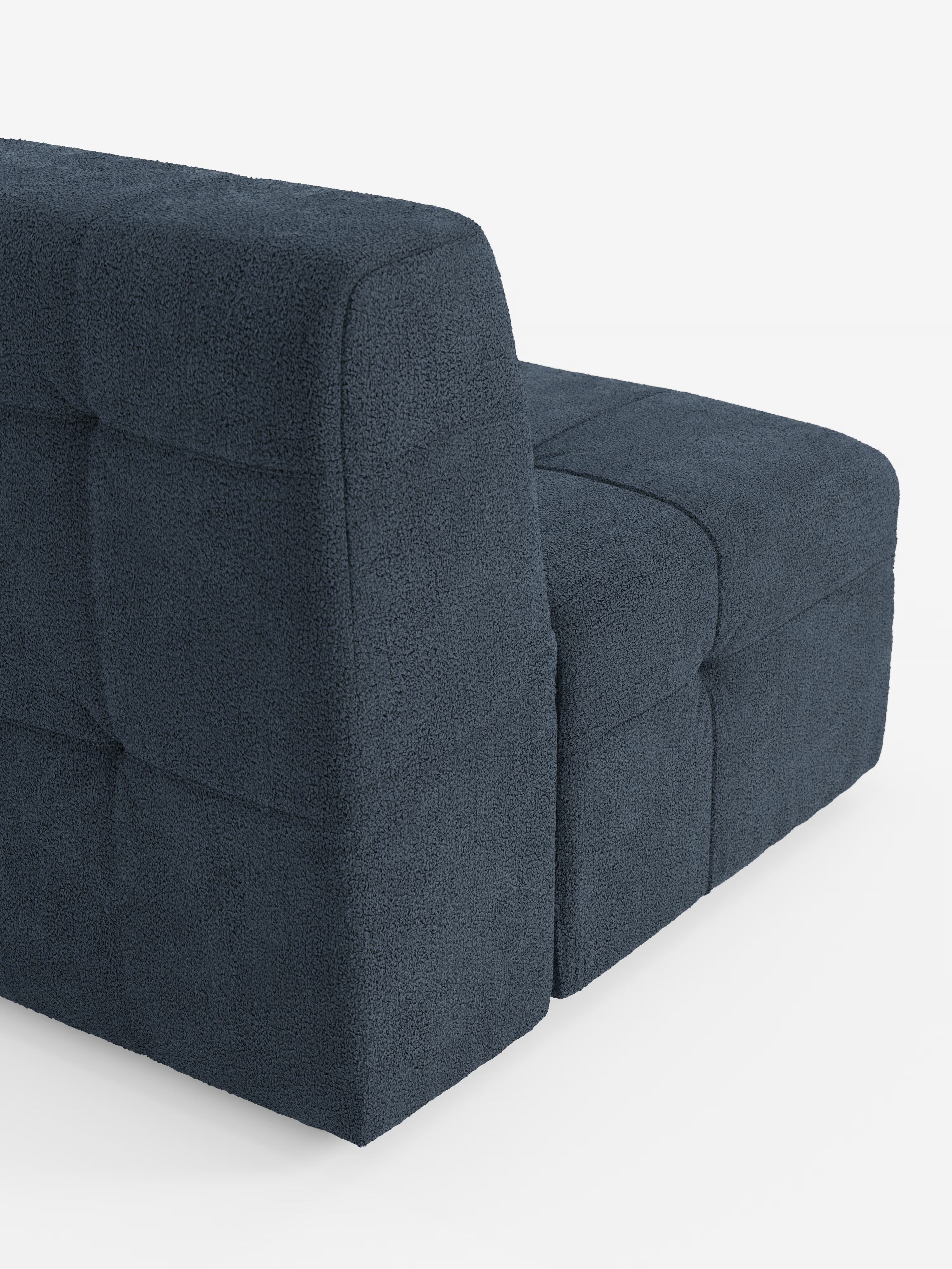 Una poltrona “Mosaic modulo” di Divani.Store, di colore blu scuro e larga 77 cm, è raffigurata su uno sfondo bianco. Rivestito in tessuto bouclé antimacchia T21 con dettagli capitonné (imbottitura a quadratini), questo divano modulare presenta un design raffinato dalle linee pulite, uno schienale basso e due sezioni a vista disposte a forma di L, che richiamano lo stile sofisticato della poltrona.