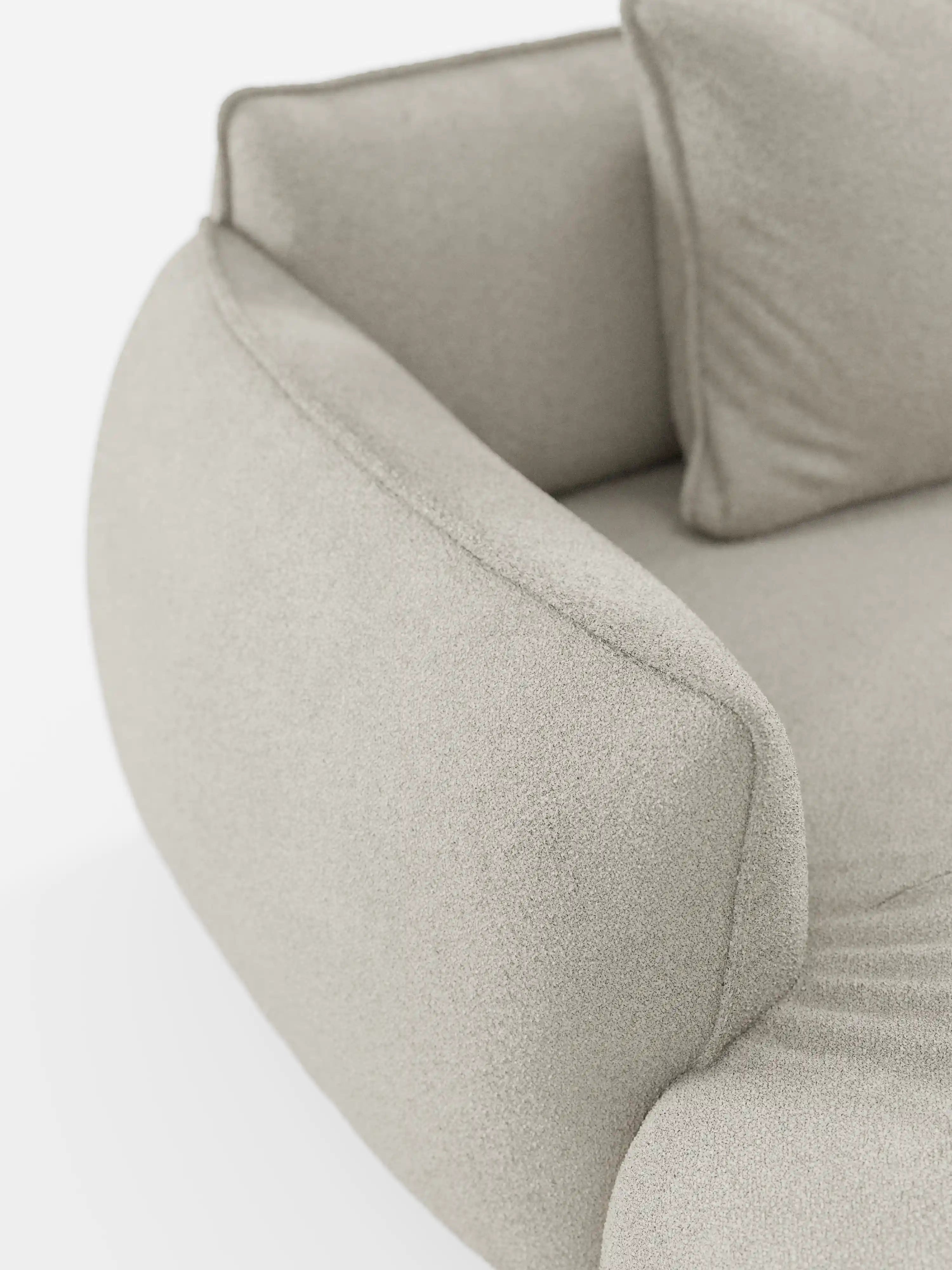 Primo piano del divano angolare panoramico componibile Nimbus con penisola e angolo in tessuto smacchiabile T33 di Divani.Store, caratterizzato da un moderno tessuto beige chiaro con una finitura morbida e testurizzata. Il bracciolo liscio e arrotondato e il morbido cuscino coordinato risaltano sullo sfondo bianco e pulito, sottolineando l’eleganza minimalista di questo divano componibile di produzione italiana.