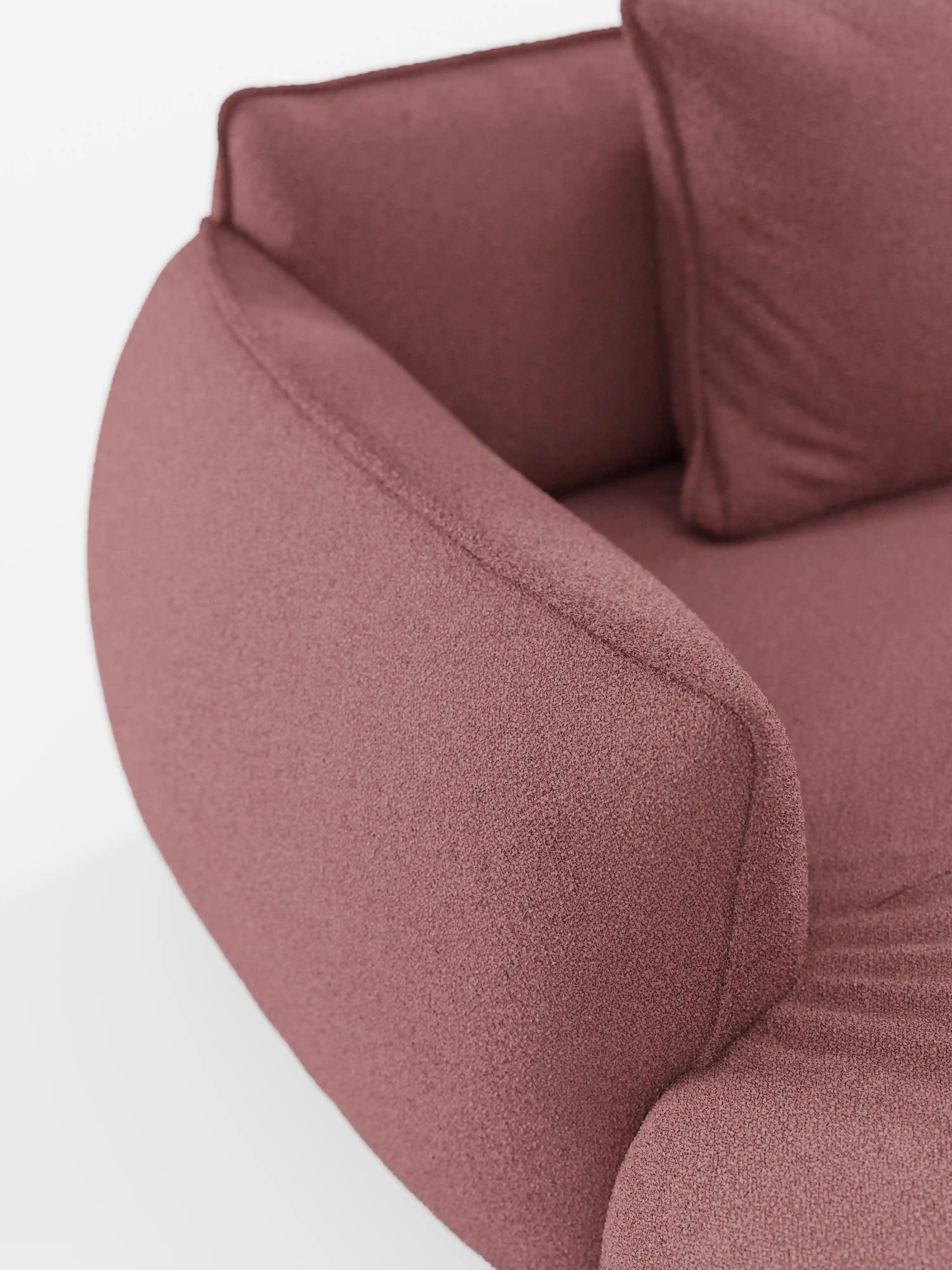 Un primo piano del divano angolare panoramico componibile Nimbus con penisola e angolo in tessuto smacchiabile T33 di Divani.Store, caratterizzato da un design curvo e contemporaneo rivestito in tessuto testurizzato color rosa antico, mette in risalto un bracciolo, una seduta imbottita e un cuscino coordinato su uno sfondo bianco.