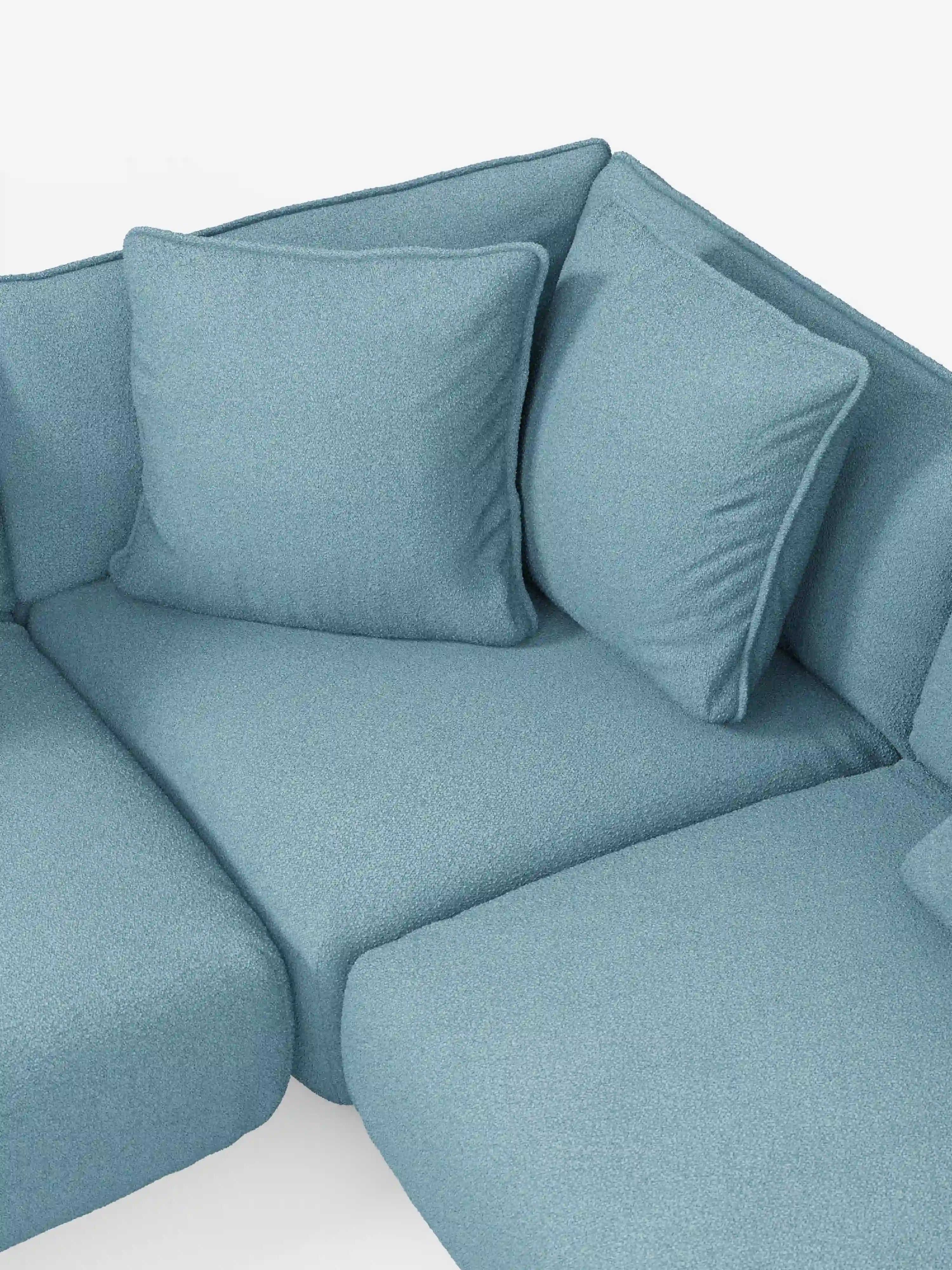 Primo piano del divano angolare panoramico componibile Nimbus con penisola e angolo in tessuto antimacchia T33 di Divani.Store, rivestito in un morbido tessuto azzurro resistente alle macchie. L’immagine mette in risalto i morbidi cuscini di seduta e i due grandi cuscini quadrati dello schienale, tutti in tinta. Realizzato in Italia, questo divano presenta un design moderno ed è fotografato su uno sfondo bianco a tinta unita.