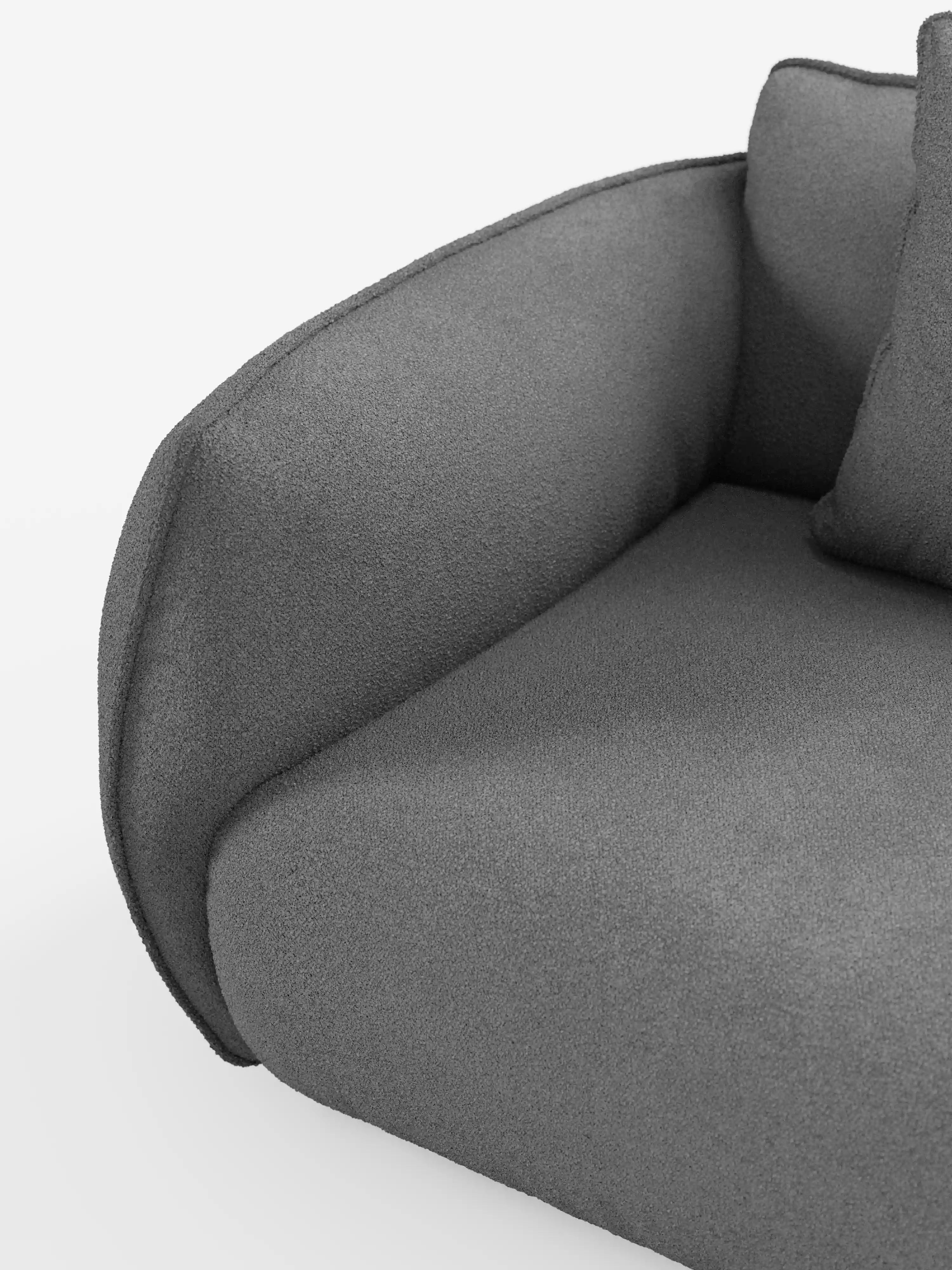 Primo piano del divano angolare con penisola componibile Nimbus di Divani.Store, che mette in risalto i braccioli e la seduta moderni, di colore grigio scuro, dalla silhouette sinuosa. Il divano è rivestito in morbido tessuto T33 effetto cotone, resistente alle macchie, per un comfort ancora maggiore. Un cuscino coordinato è parzialmente visibile sulla seduta, su uno sfondo bianco a tinta unita.