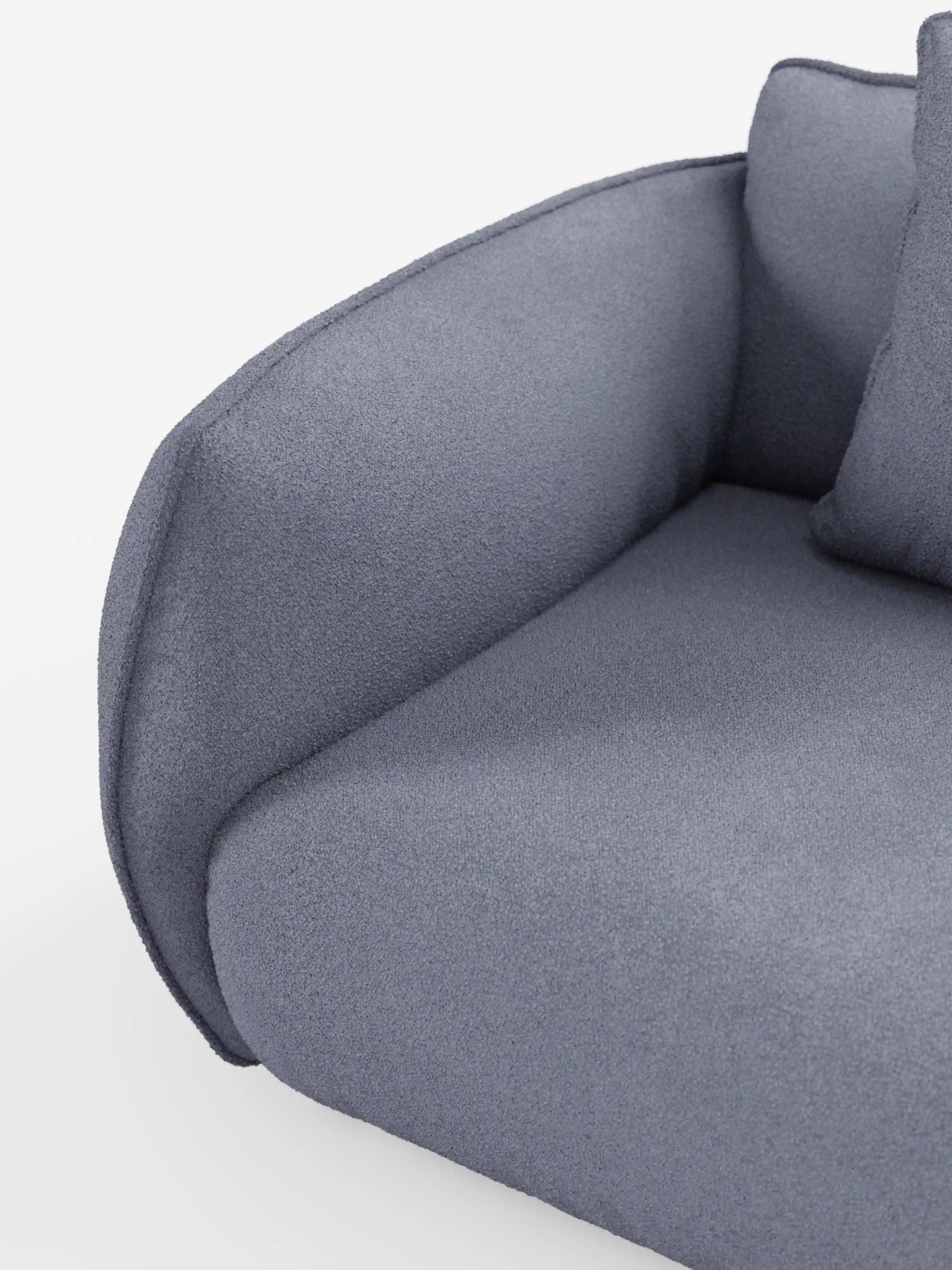 Primo piano del divano angolare con penisola componibile Nimbus di Divani.Store, rivestito in morbido tessuto T33 effetto cotone resistente alle macchie. L'immagine mette in risalto i bordi lisci e arrotondati del bracciolo curvo, del cuscino della seduta e di parte del cuscino dello schienale, esaltando il design minimalista e il rivestimento grigio testurizzato su uno sfondo bianco a tinta unita.