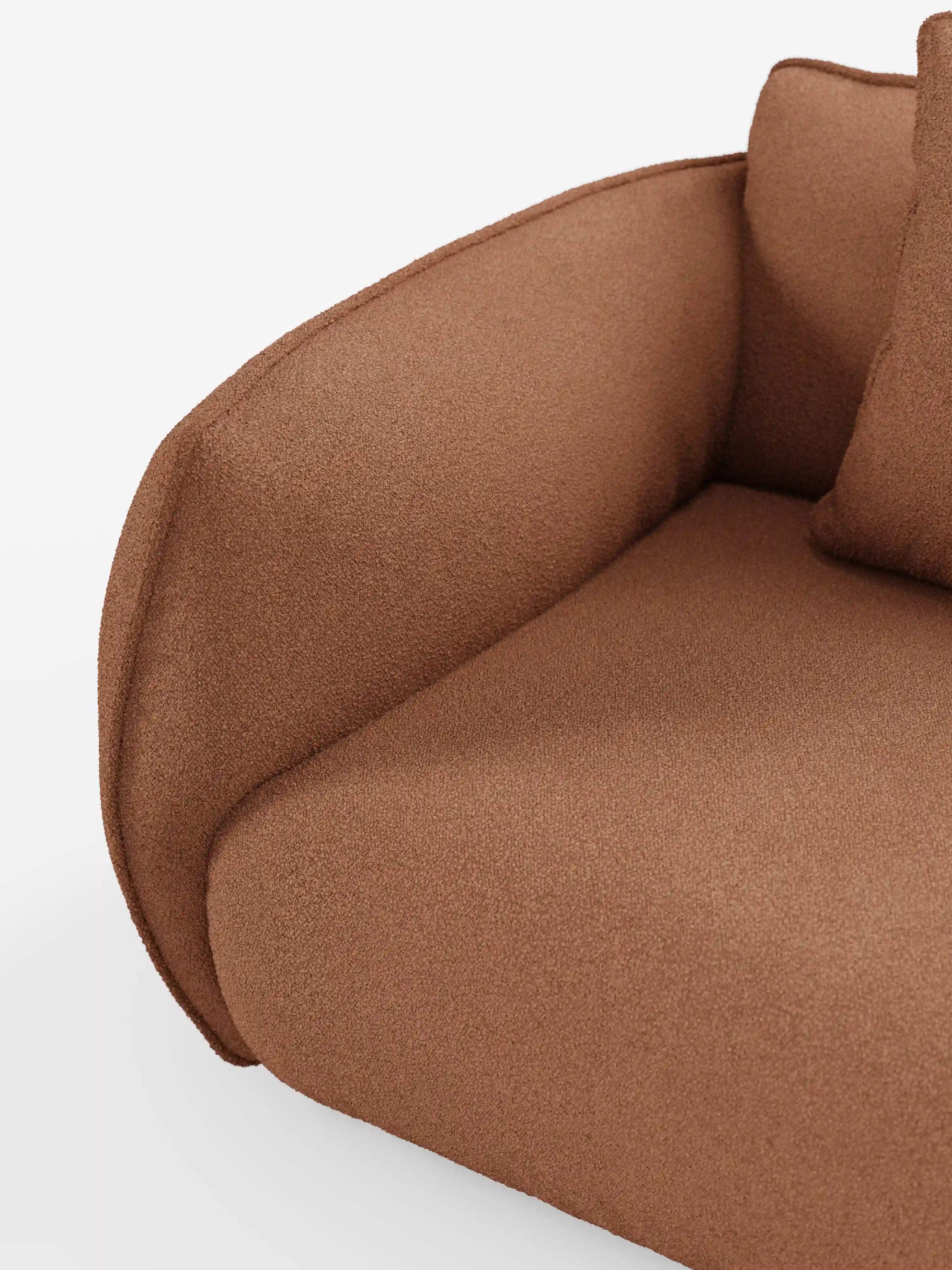 Un primo piano del divano angolare con penisola componibile Nimbus di Divani.Store mette in risalto il suo bracciolo liscio e arrotondato e il cuscino abbinato. Il rivestimento è realizzato in tessuto T33 di colore marrone-rossastro, resistente alle macchie e dalla morbida consistenza simile al cotone, mentre le linee pulite e l’imbottitura soffice completano il design moderno su uno sfondo bianco a tinta unita.