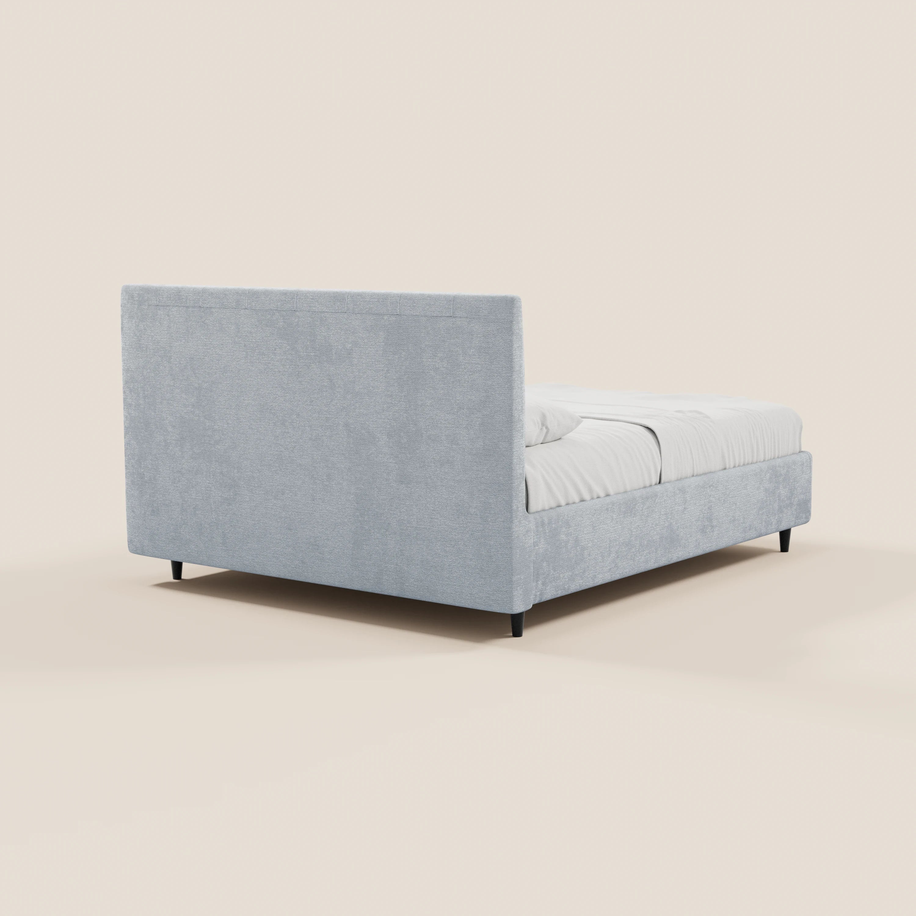 Il letto imbottito ONYX con contenitore e testiera verticale in tessuto Oeko-Tex® di Letti.store presenta una struttura e una testiera imbottite di colore grigio chiaro. Nella foto, ripreso da dietro, poggia su gambe corte di colore scuro, con biancheria da letto di un bianco brillante che risalta su uno sfondo bianco sporco.